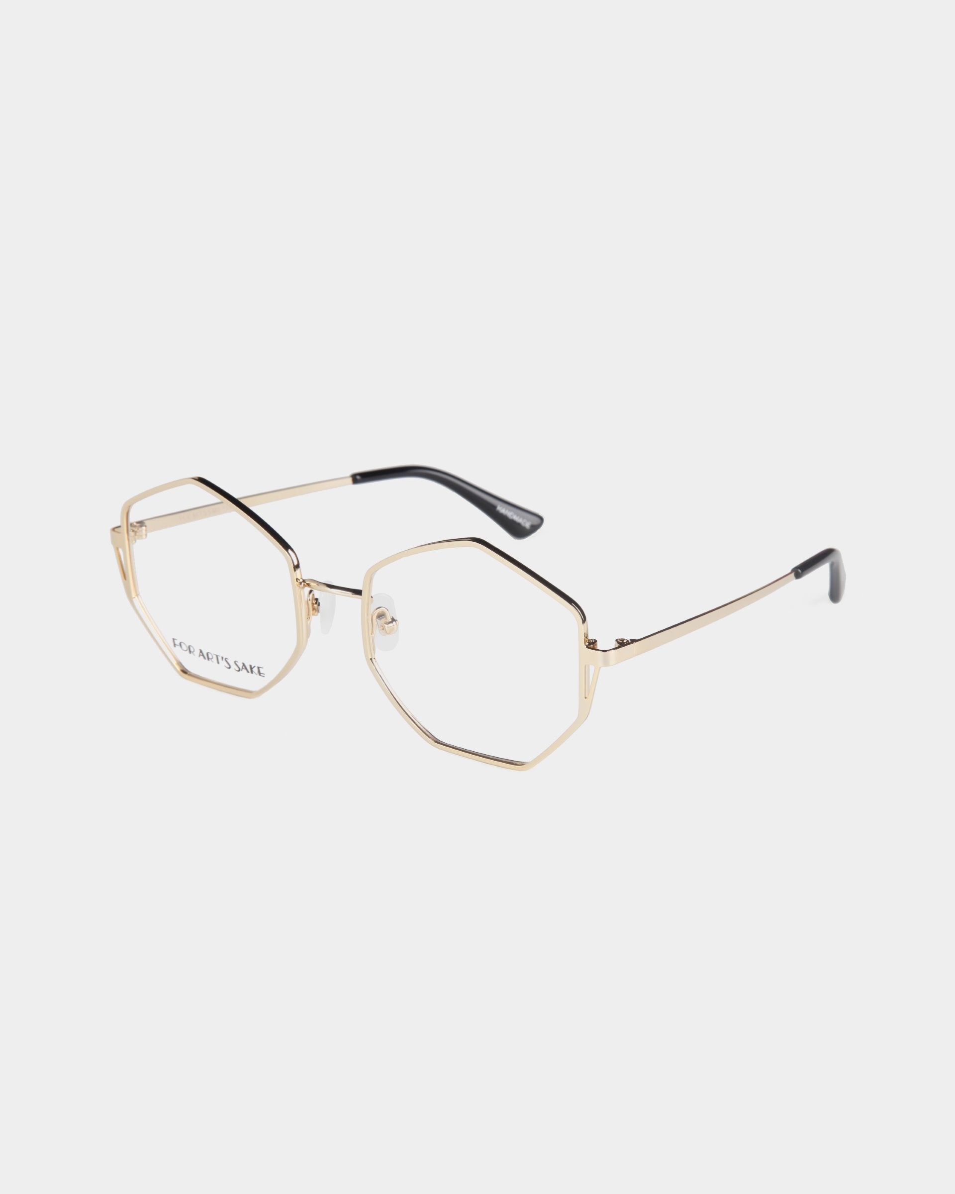 A pair of geometric gold-framed eyeglasses with heptagon-shaped lenses, black temple tips, and adjustable jade nose pads, displayed on a white background. The product name is Antidote by For Art's Sake®.