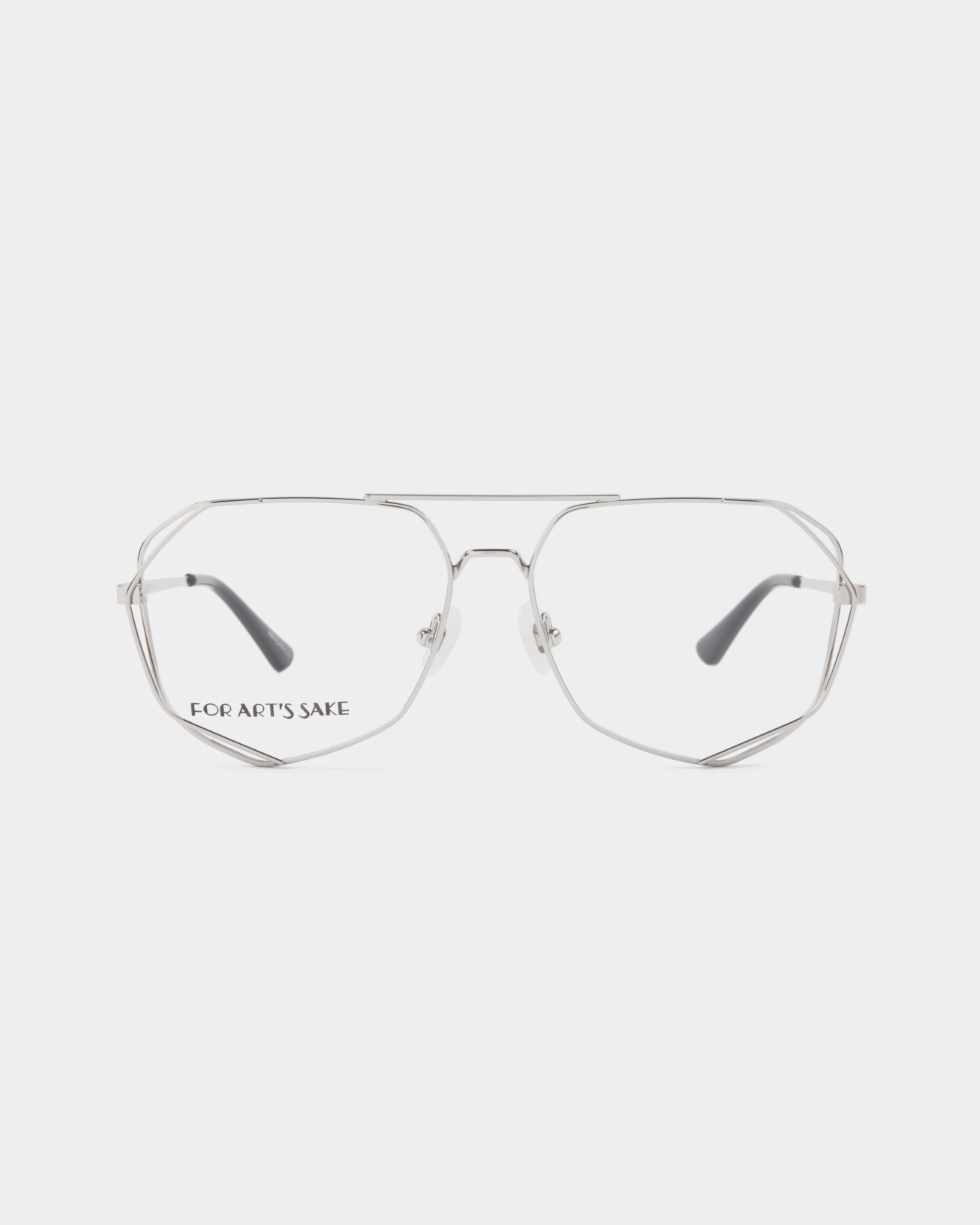 A pair of silver metal eyeglasses with thin, geometric stainless steel frames and clear lenses. The words "FOR ART'S SAKE" are printed on the left lens. The glasses have adjustable nose pads and black ear tips. With a plain white background, these stylish specs offer a Blue Light Filter option for added protection. These are the Genius eyeglasses by For Art's Sake®.