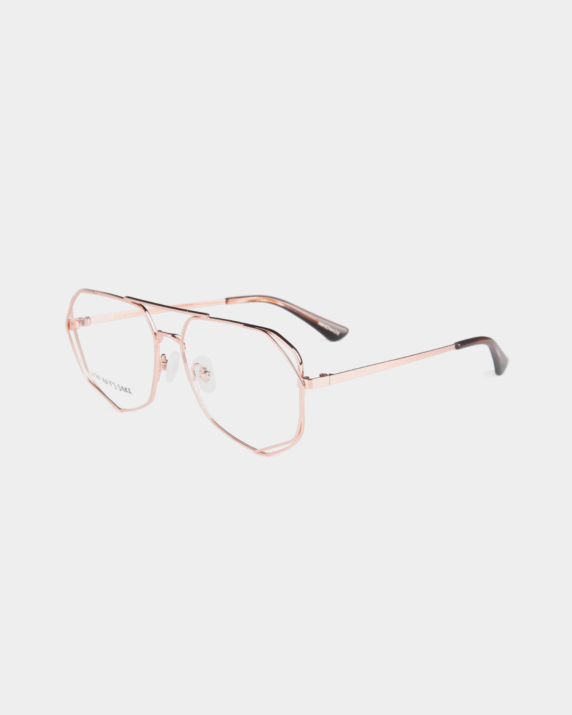 A pair of aviator-style Genius eyeglasses by For Art&#39;s Sake® with thin, rose gold metal frames and clear lenses featuring black tips on the temple arms. The design includes a double bridge and adjustable nose pads, offering the option for a Blue Light Filter. The background is white.