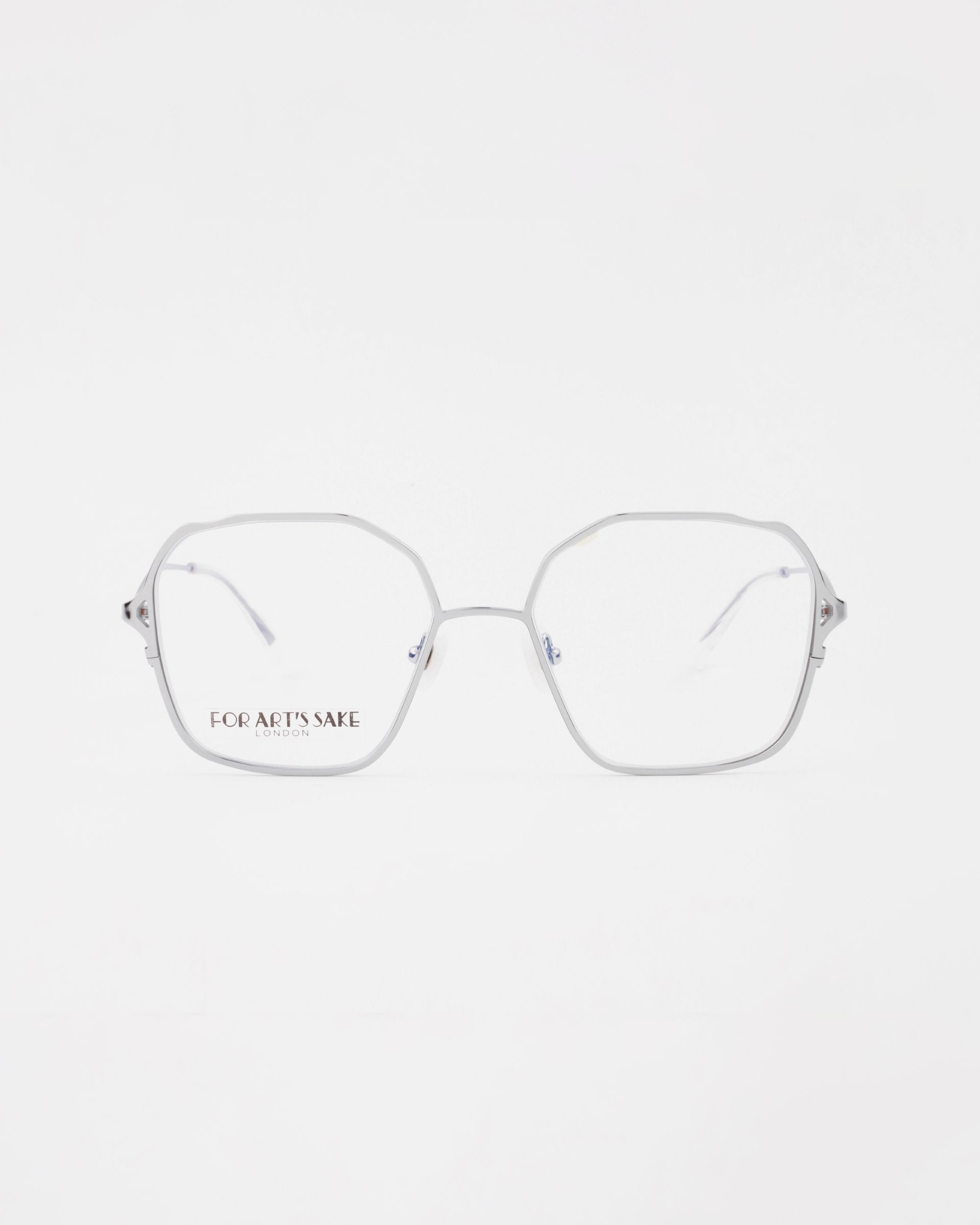A pair of silver Mimi eyeglasses with octagonal frames and clear lenses, featuring an 18-karat gold-plated bridge, set against a plain white background. The brand name &quot;FOR ART&#39;S SAKE&quot; is printed on the left lens in black letters. The glasses are available with a prescription service.