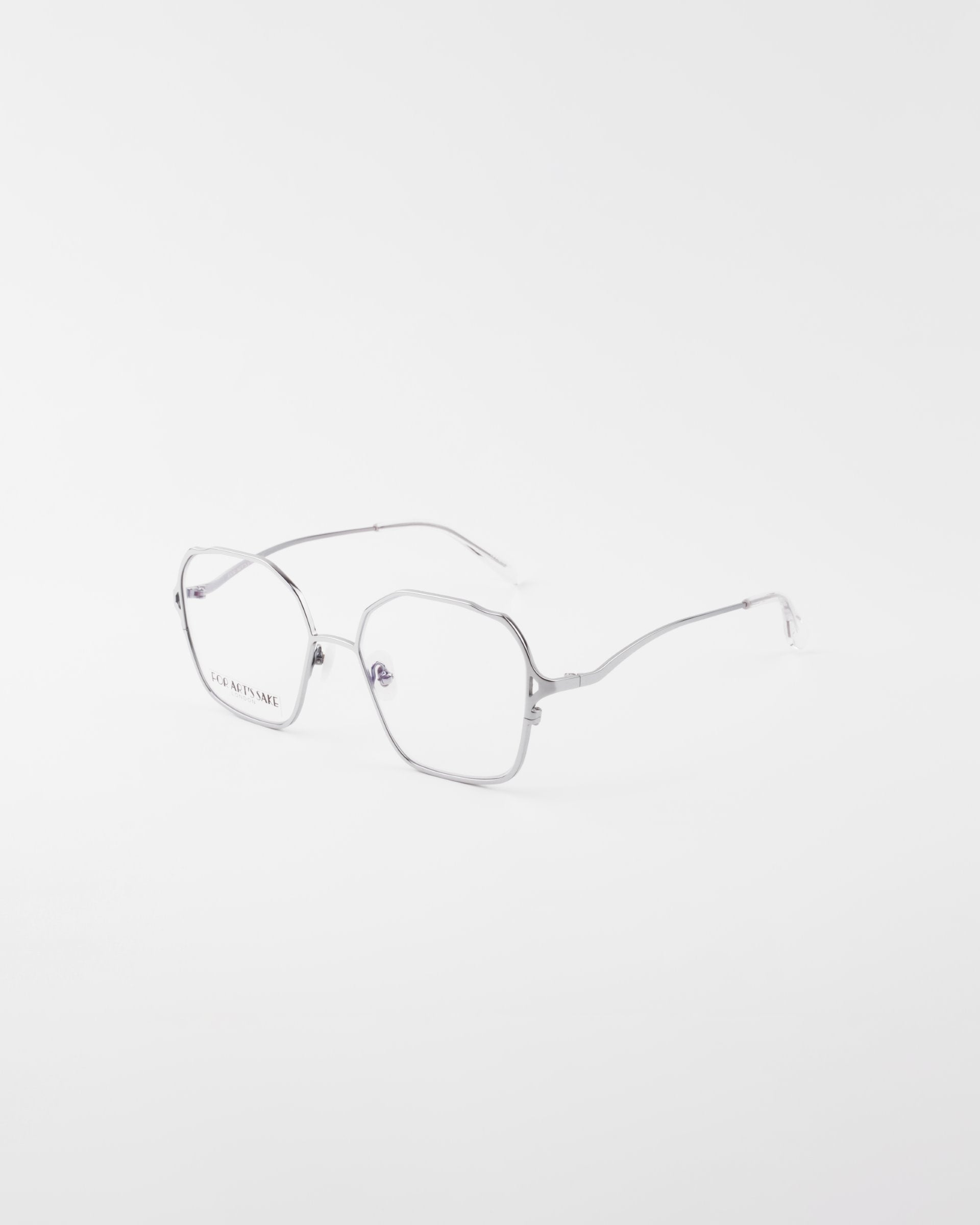 A pair of Mimi eyeglasses from For Art&#39;s Sake® with thin, 18-karat gold-plated frames and clear lenses is displayed on a plain white background. The glasses have a modern, minimalist design with hexagonal-shaped lenses and slim temples.