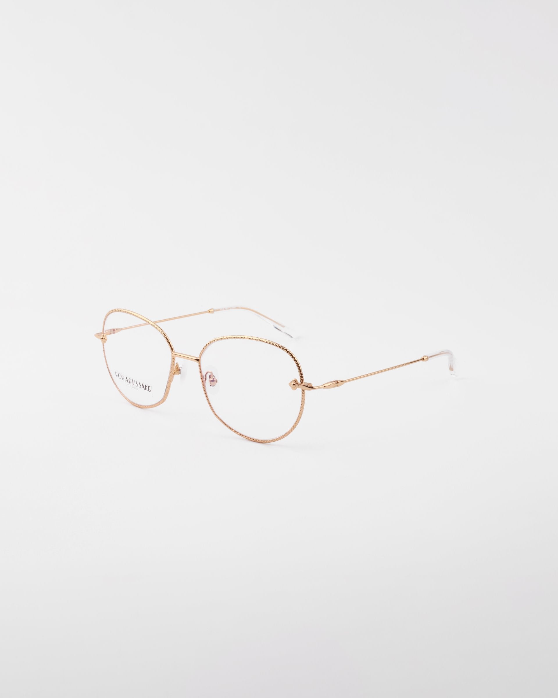 A pair of gold-framed, round eyeglasses with clear lenses is set against a plain white background. The delicate, handmade Jasmine eyewear by For Art&#39;s Sake® features thin temples with a subtle texture, and the nose pads are transparent. The frame is crafted from gold-plated stainless steel for added elegance and durability.