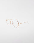 A pair of gold-framed, round eyeglasses with clear lenses is set against a plain white background. The delicate, handmade Jasmine eyewear by For Art's Sake® features thin temples with a subtle texture, and the nose pads are transparent. The frame is crafted from gold-plated stainless steel for added elegance and durability.