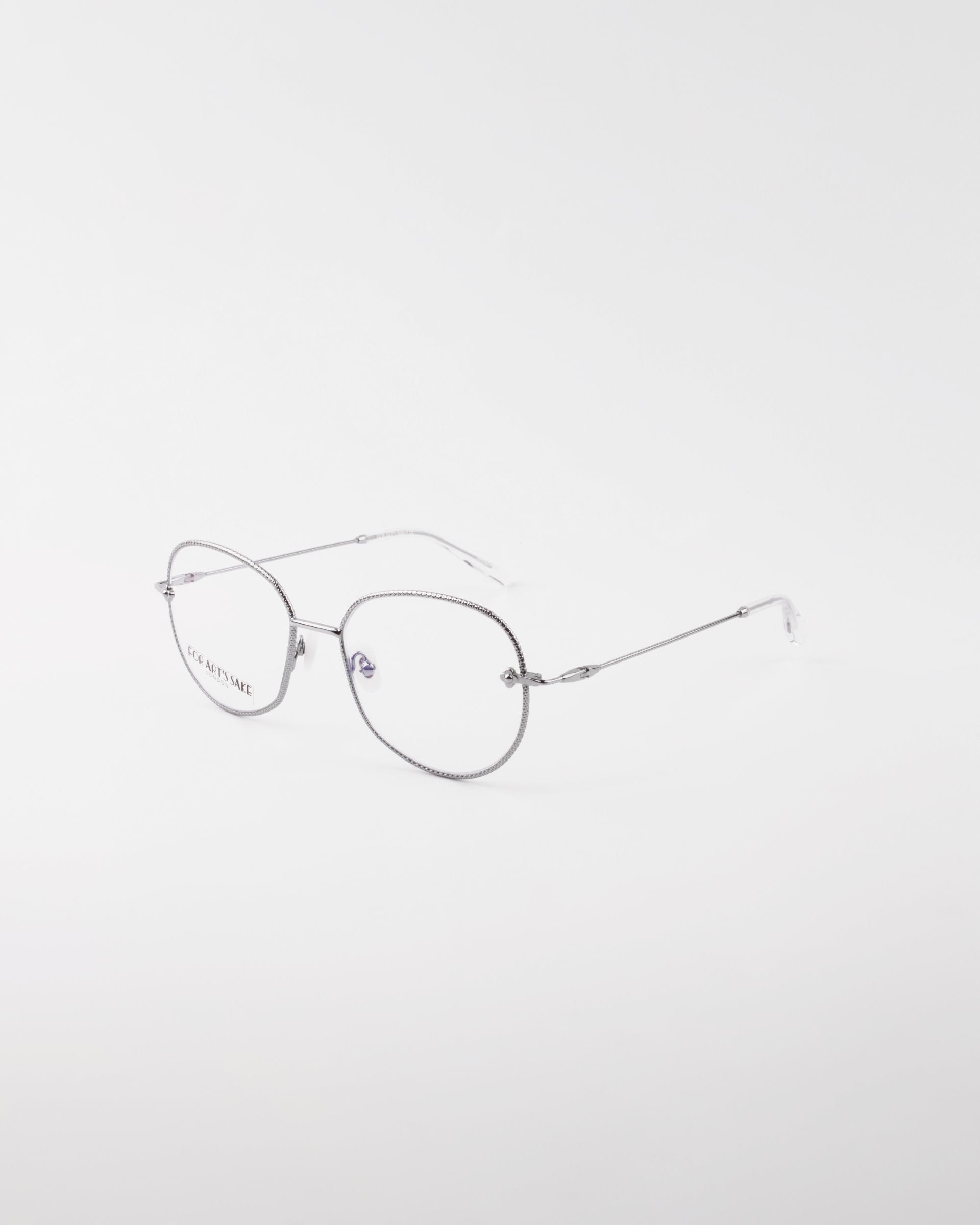 A pair of thin metal-framed eyeglasses with round lenses. The frames are gold-plated stainless steel, and the glasses are positioned at an angle against a plain white background. The minimalistic design gives this piece of handmade For Art&#39;s Sake® Jasmine eyewear an elegant and sleek appearance.
