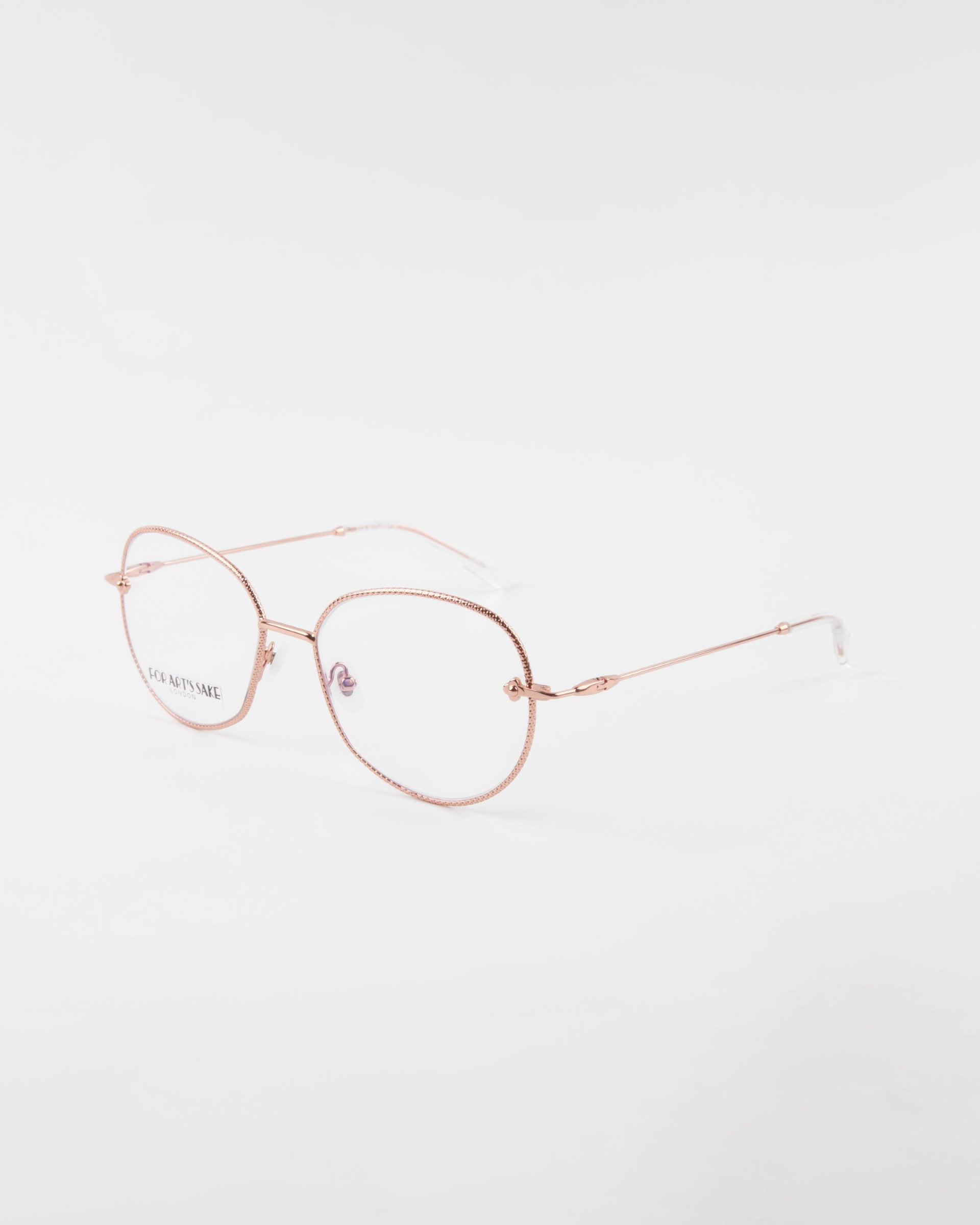 A pair of Jasmine eyeglasses by For Art&#39;s Sake® with a thin and delicate frame is displayed against a white background. The handmade eyewear boasts ovoid lenses, clear nose pads, and a minimalist, elegant design. Crafted from gold-plated stainless steel, the arms are straight with a slight curve at the ends.
