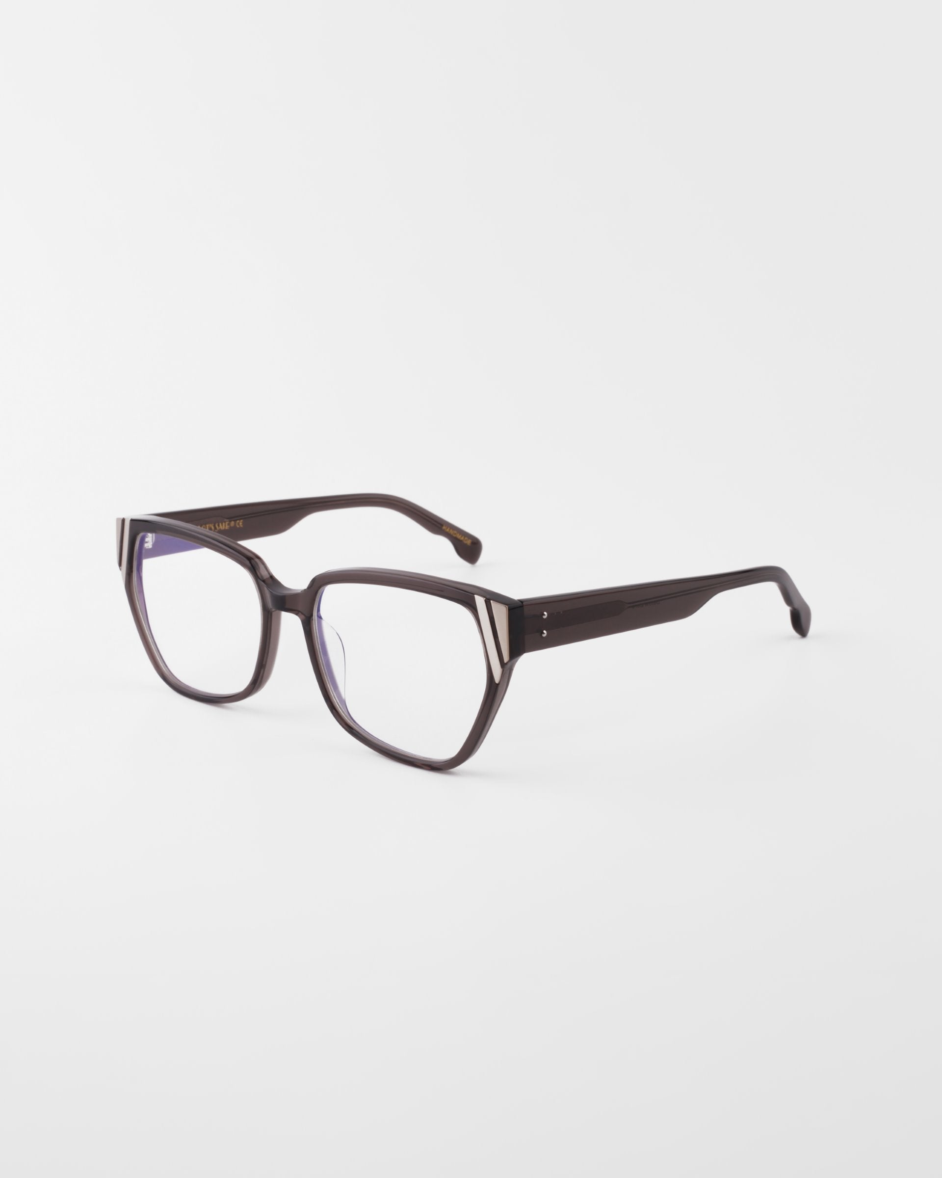 The Below Zero eyeglasses from For Art's Sake® feature square-shaped, dark acetate frames with clear lenses, subtle metal accents at the temples, and tapering arms. They sit on a white background and offer a modern unisex style.