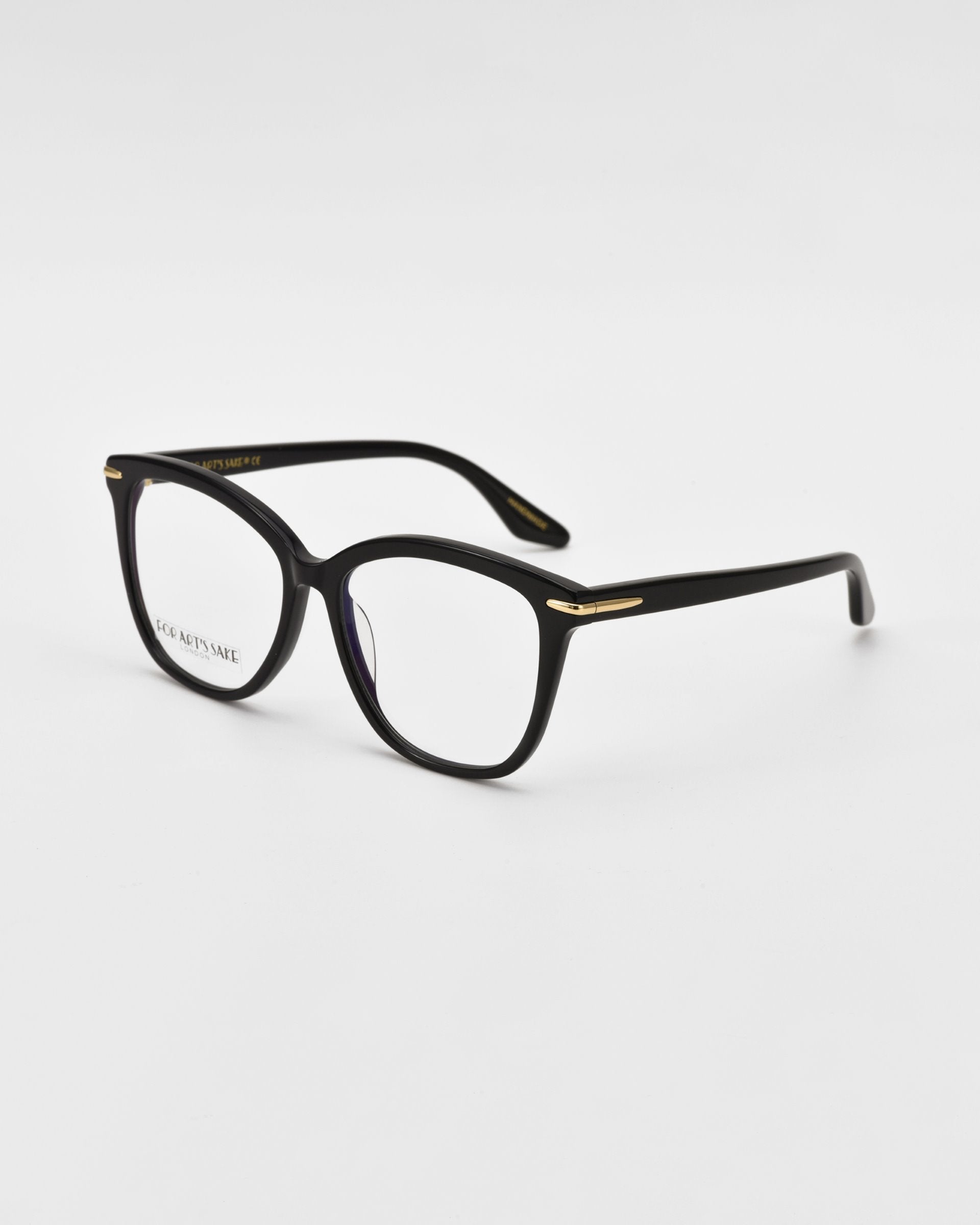 A pair of black For Art&#39;s Sake® Cadenza optical glasses with rounded rectangular lenses and gold accents on the hinges. The glasses are placed at an angle on a clean, white background.