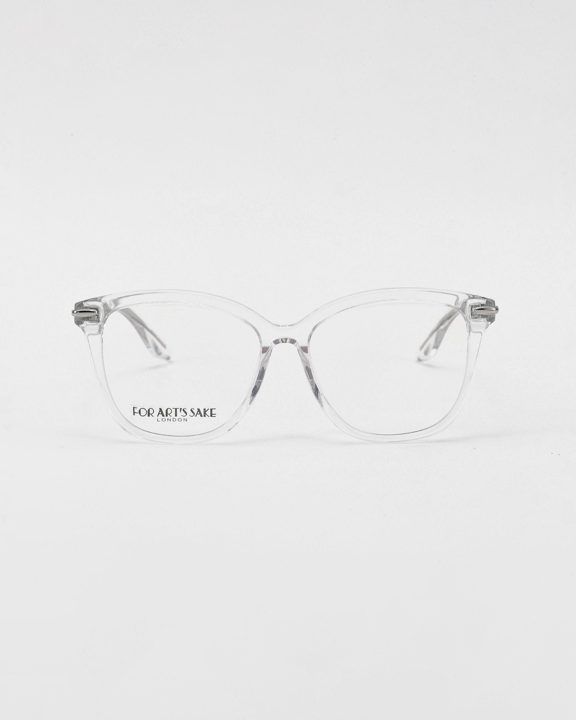 A pair of transparent For Art&#39;s Sake® optical glasses with rectangular lenses is centered against a plain white background. The text &quot;FOR ART&#39;S SAKE&quot; appears on one lens near the bridge. The Cadenza glasses have a minimalist and modern design, offering an option for prescription service.
