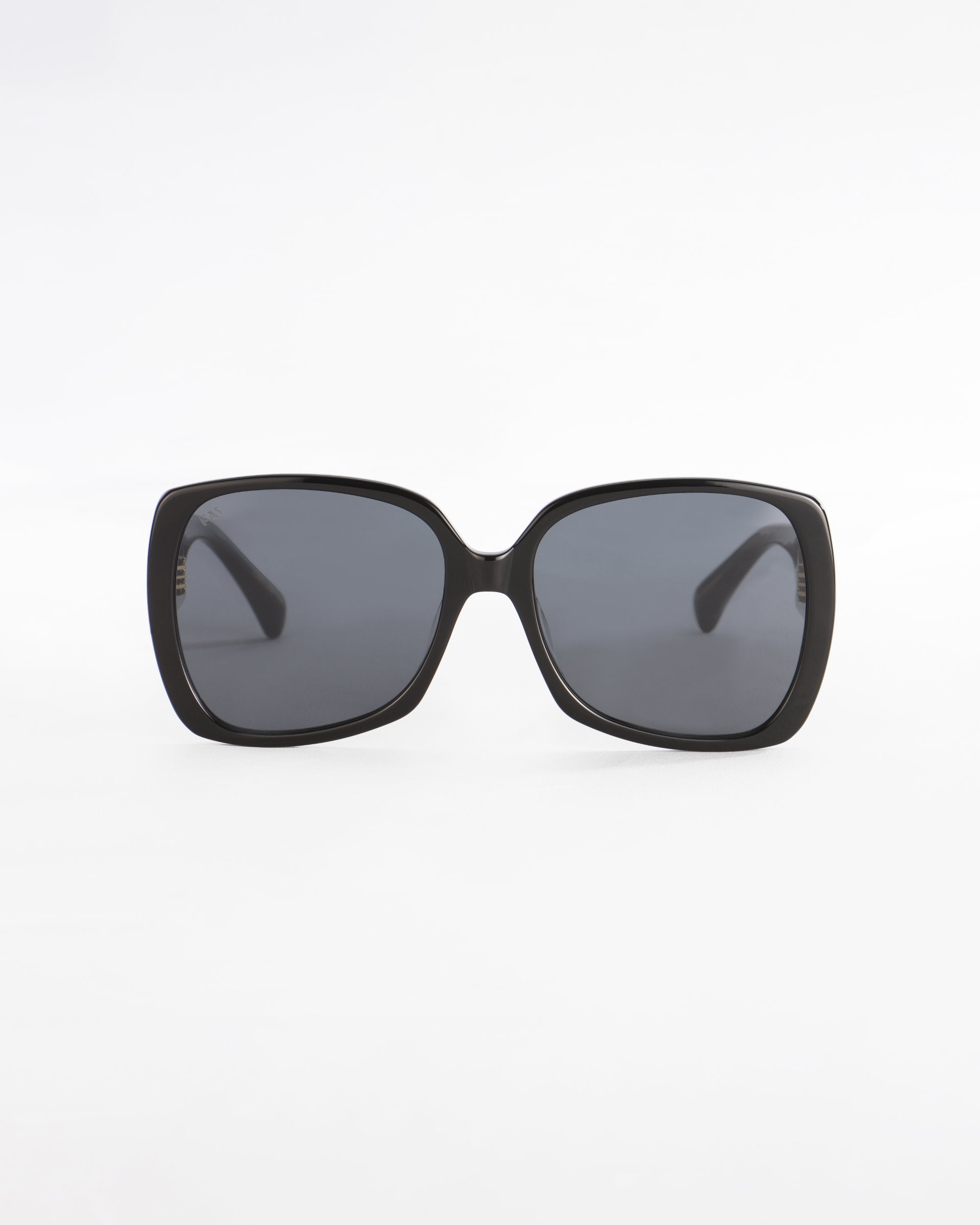 A pair of black, oversized square Odyssey sunglasses by For Art&#39;s Sake® with dark tinted, lightweight nylon lenses is displayed against a plain white background. The design is simple and modern, featuring thick frames made from plant-based acetate and wide arms.