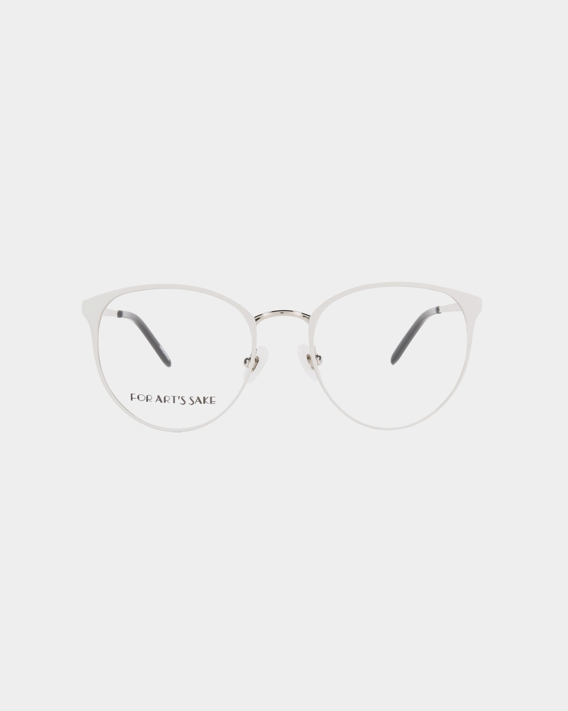 A pair of **For Art&#39;s Sake® Olivia Grey** minimalist eyeglasses with round, silver metal frames. The glasses have clear lenses and sleek temples with grey tips. Featuring blue light filter technology, the words &quot;FOR ART&#39;S SAKE&quot; are printed on the left lens. The background is plain white.