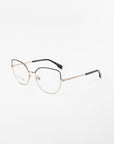 A pair of Ophelia by For Art's Sake® eyeglasses with a gold-colored frame and black earpieces. The frame features a subtle chain-like design on the temples, and the clear lenses come with a blue light filter. The glasses are set against a plain white background.