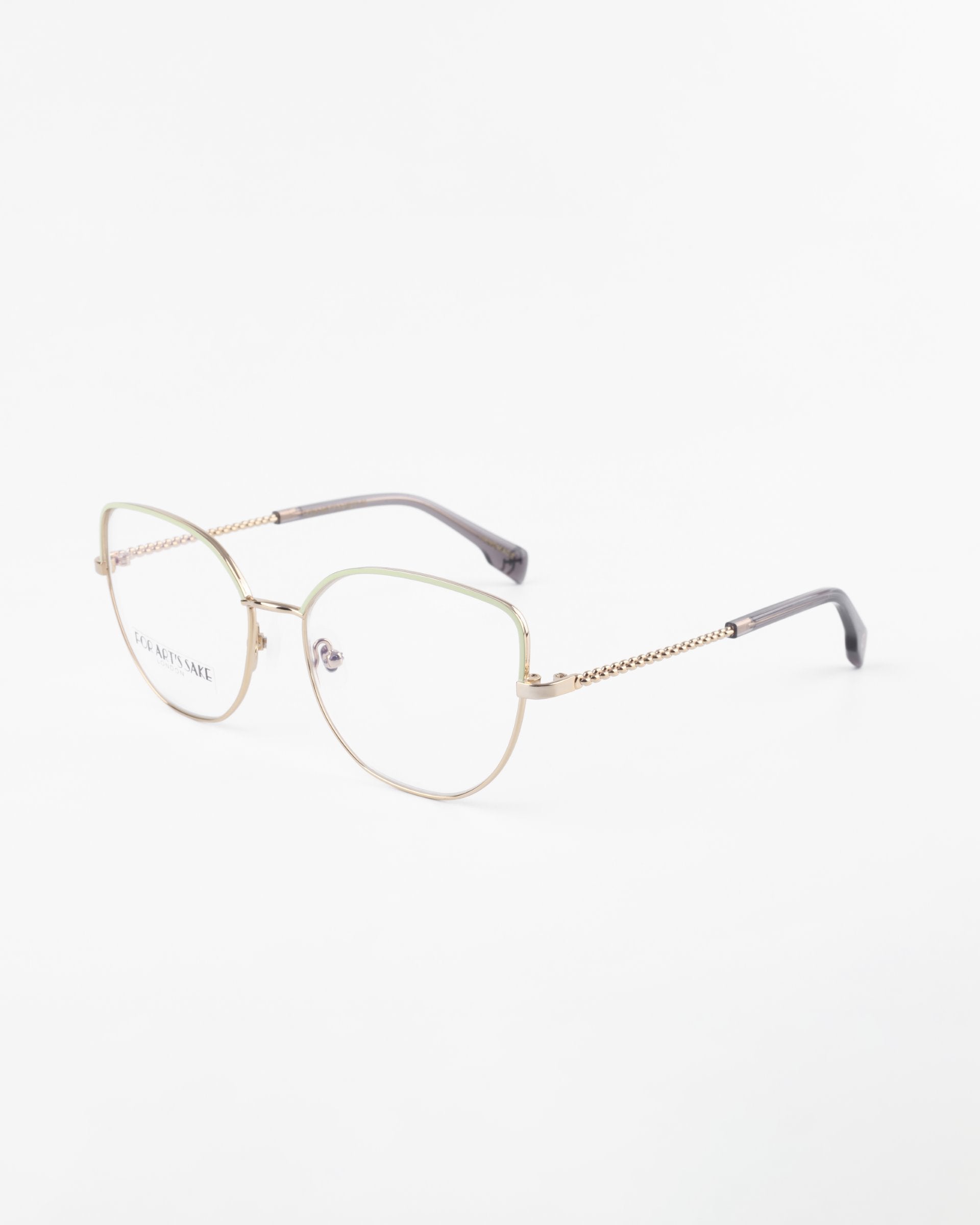 A pair of gold-rimmed Ophelia eyeglasses by For Art&#39;s Sake® with a slightly rounded square shape is shown against a plain white background. The glasses feature blue light filter lenses and a delicate chain-like design on the temples, transitioning to dark grey tips.
