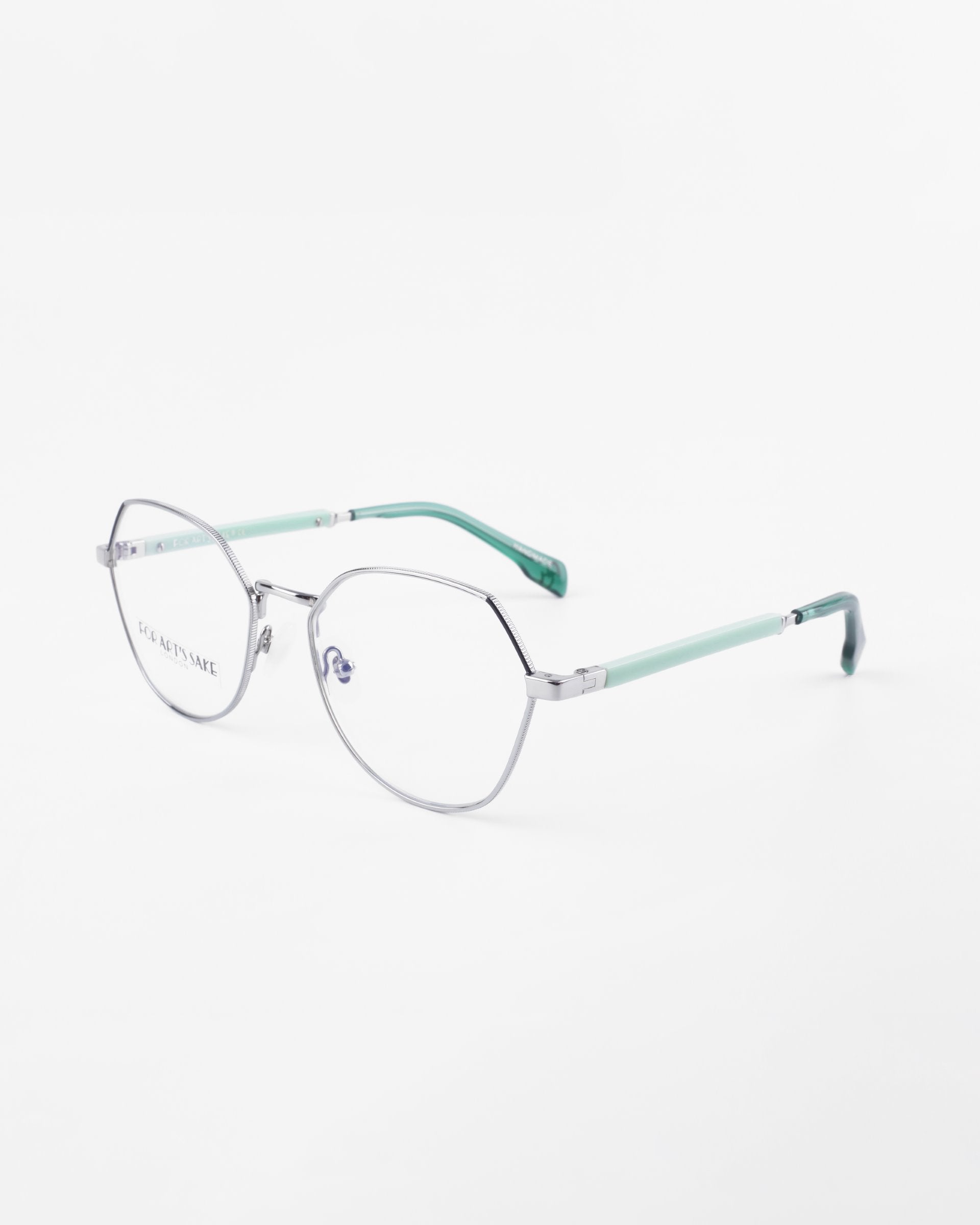 A pair of Orchard by For Art's Sake® eyeglasses with hexagonal silver frames and clear, prescription lenses. The arms of the glasses are light green, creating a modern and stylish look. The background is plain white, highlighting the glasses.