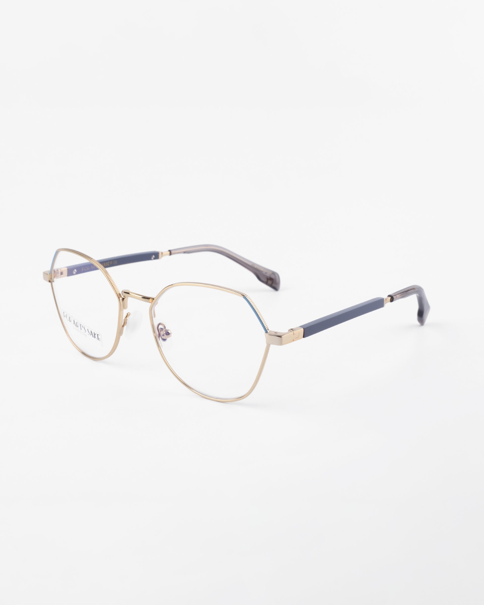 Close-up of a pair of Orchard frames by For Art&#39;s Sake® with clear prescription lenses, featuring an angular design and navy-blue accents on the tips of the arms. The glasses are positioned against a plain white background.