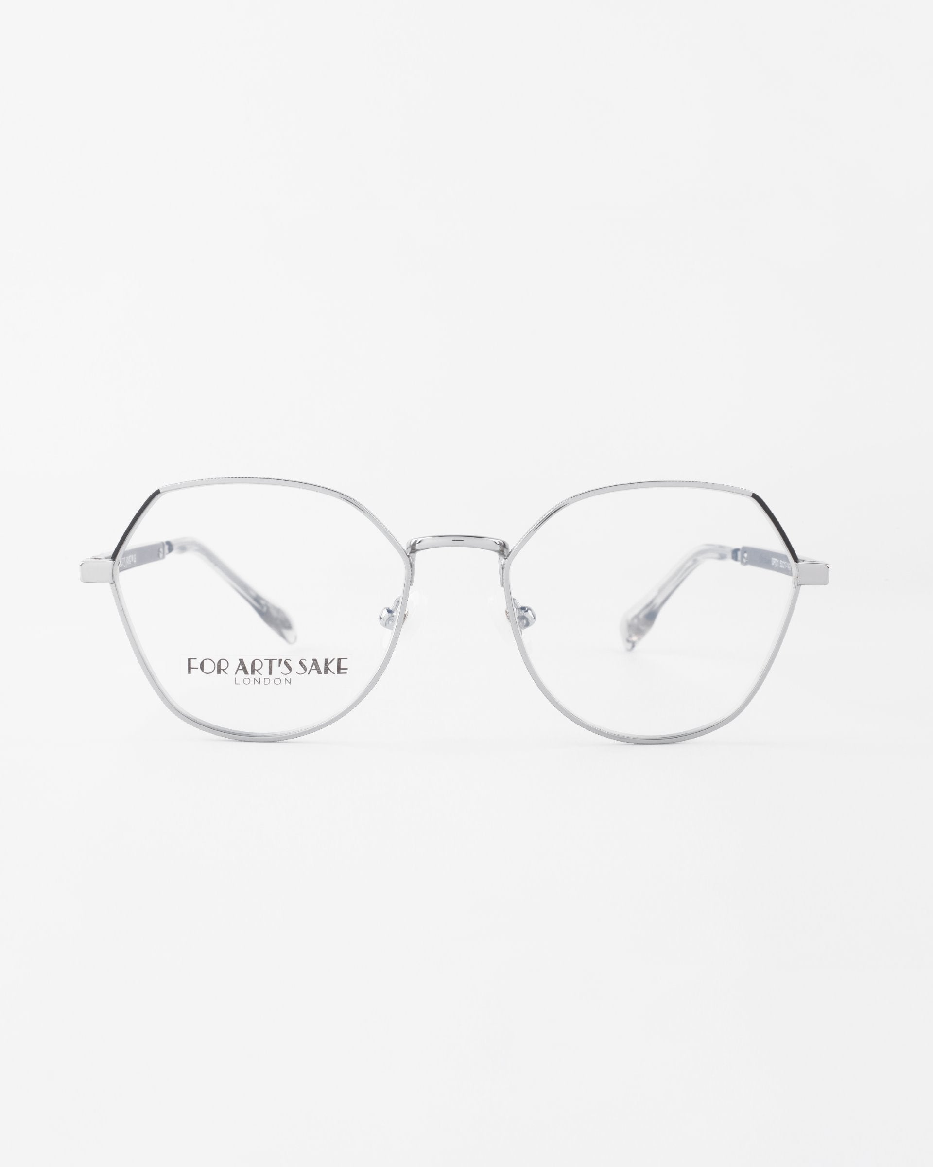 Image of a pair of sleek metal eyeglasses with a minimalist design. Featuring hexagonal gold-plated frames, clear lenses, and thin temples, the Orchard glasses offer both style and functionality. The brand name &quot;For Art&#39;s Sake®&quot; is printed in small text on the left lens. The background is a clean white.