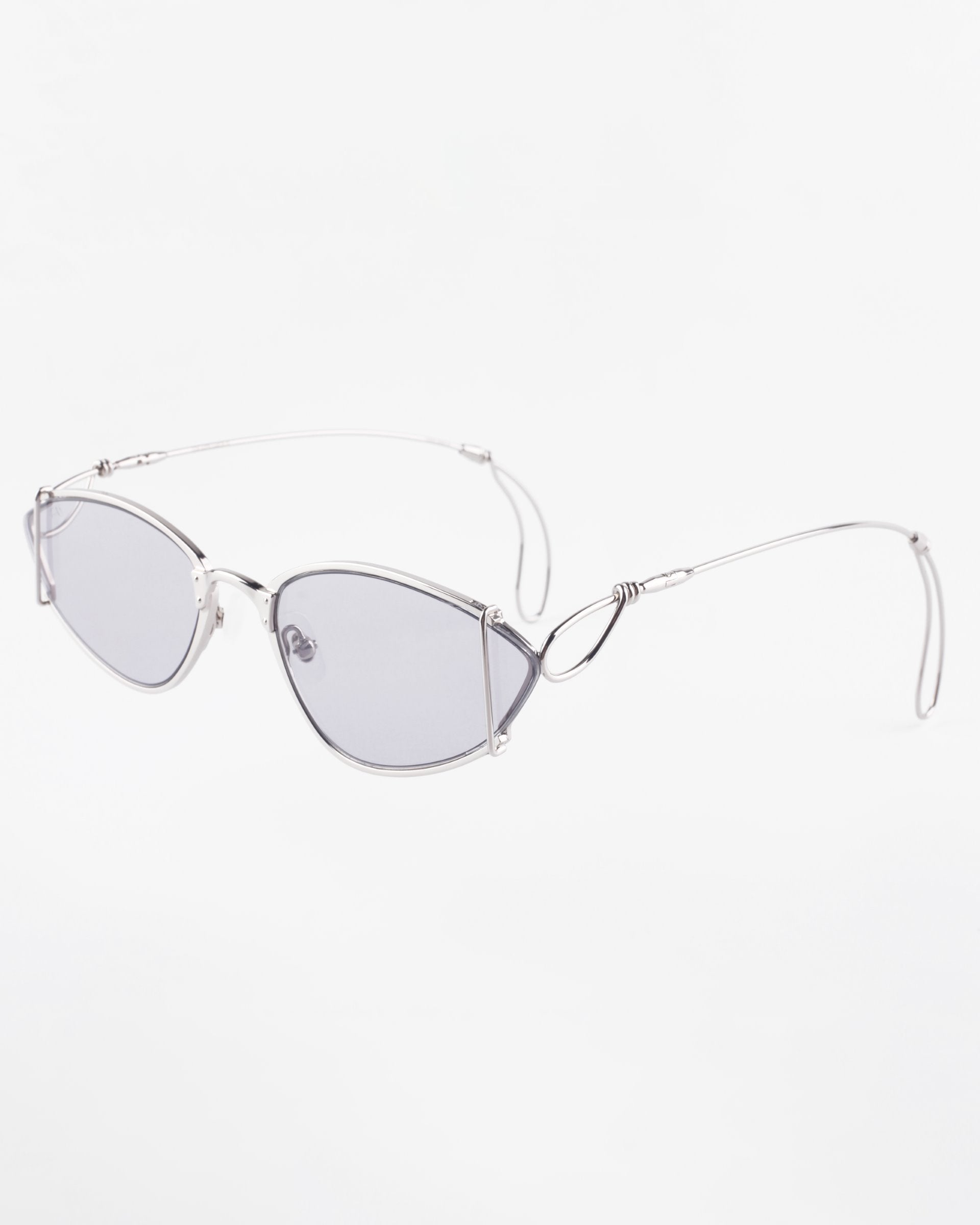 A pair of stylish, slim-framed glasses with silver wire frames and lightly tinted rectangular lenses. The Ornate glasses from For Art&#39;s Sake® have intricate wire detailing near the hinges and thin, flexible temple arms. Featuring ultra-lightweight Nylon lenses with 100% UVA &amp; UVB protection, the background is plain white.