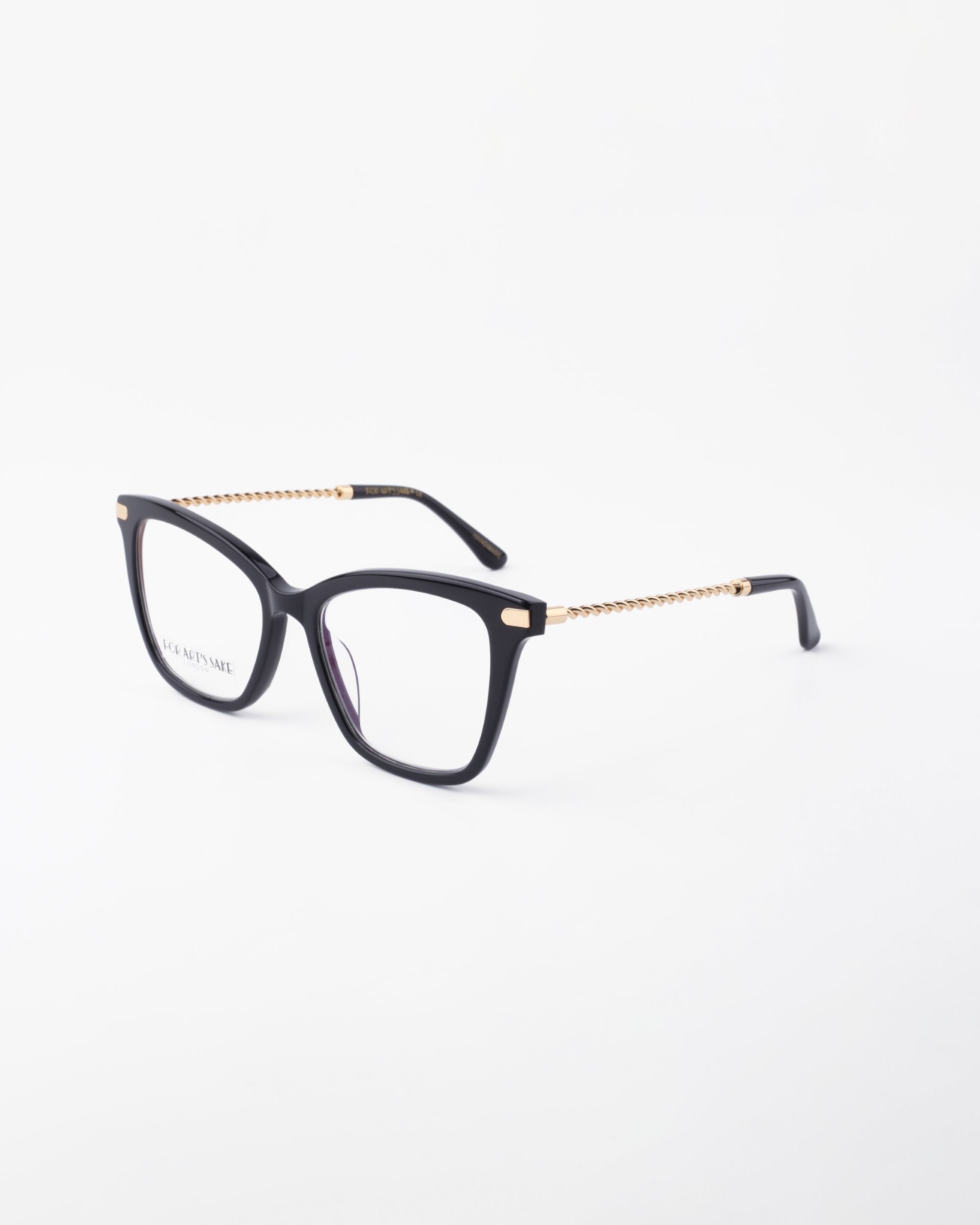 A pair of For Art's Sake® Paris Two black framed glasses with gold accents and chain-like details on the temples are positioned against a plain white background. The lenses, featuring a blue light filter, are clear, and the overall design is modern and stylish.