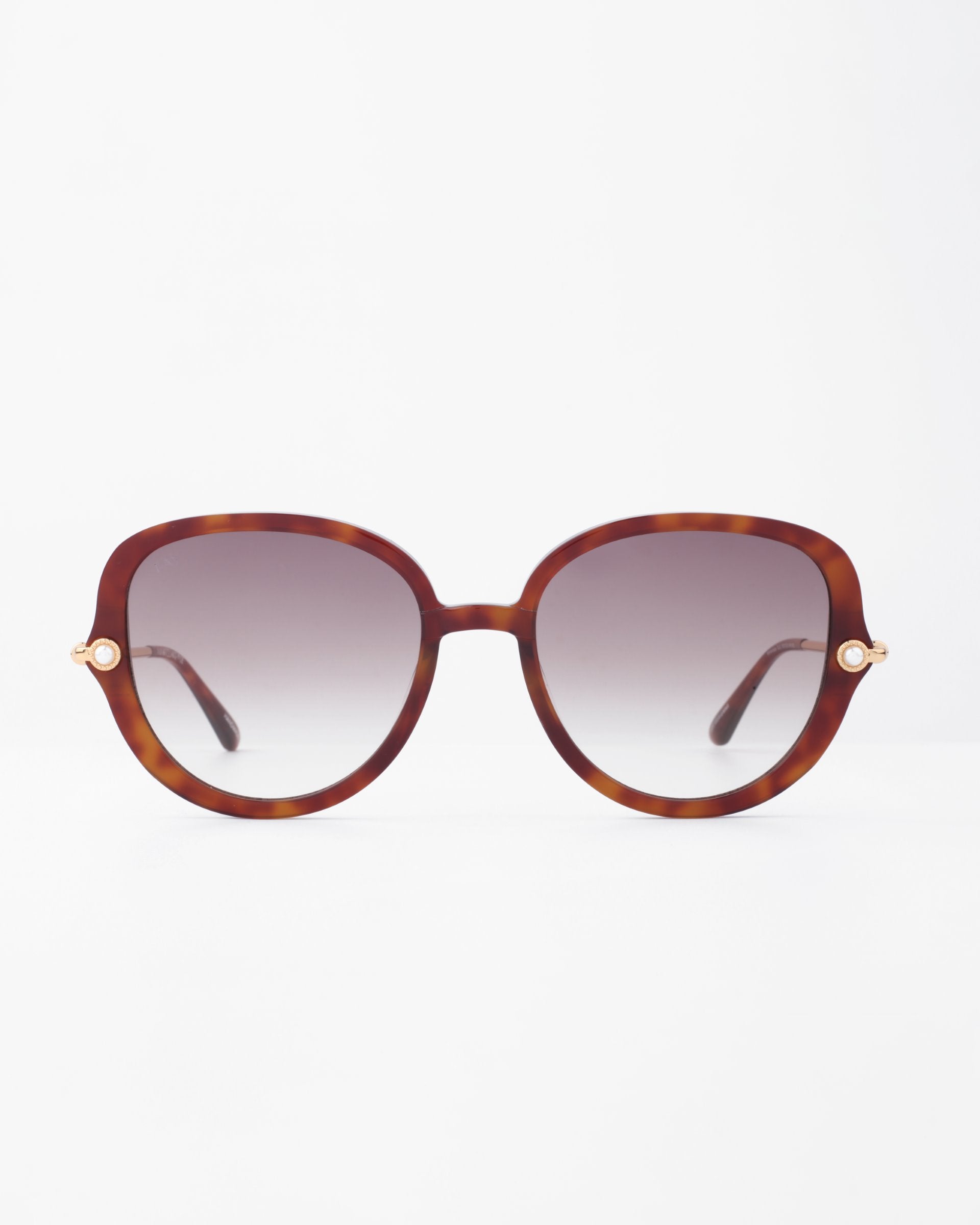 A pair of oversized, square-shaped Primrose sunglasses by For Art&#39;s Sake® with tortoiseshell frames made from plant-based acetate and gradient brown lenses is centered against a plain white background. Small handmade gold-plated accents are visible on the hinges where the temples meet the frame.