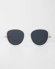 A pair of white-framed For Art's Sake® Primrose sunglasses with large, round dark lenses. Each temple is adorned with a small, handmade gold-plated decorative detail near the hinges. The glossy, smooth frame is made from plant-based acetate and the background is plain white.