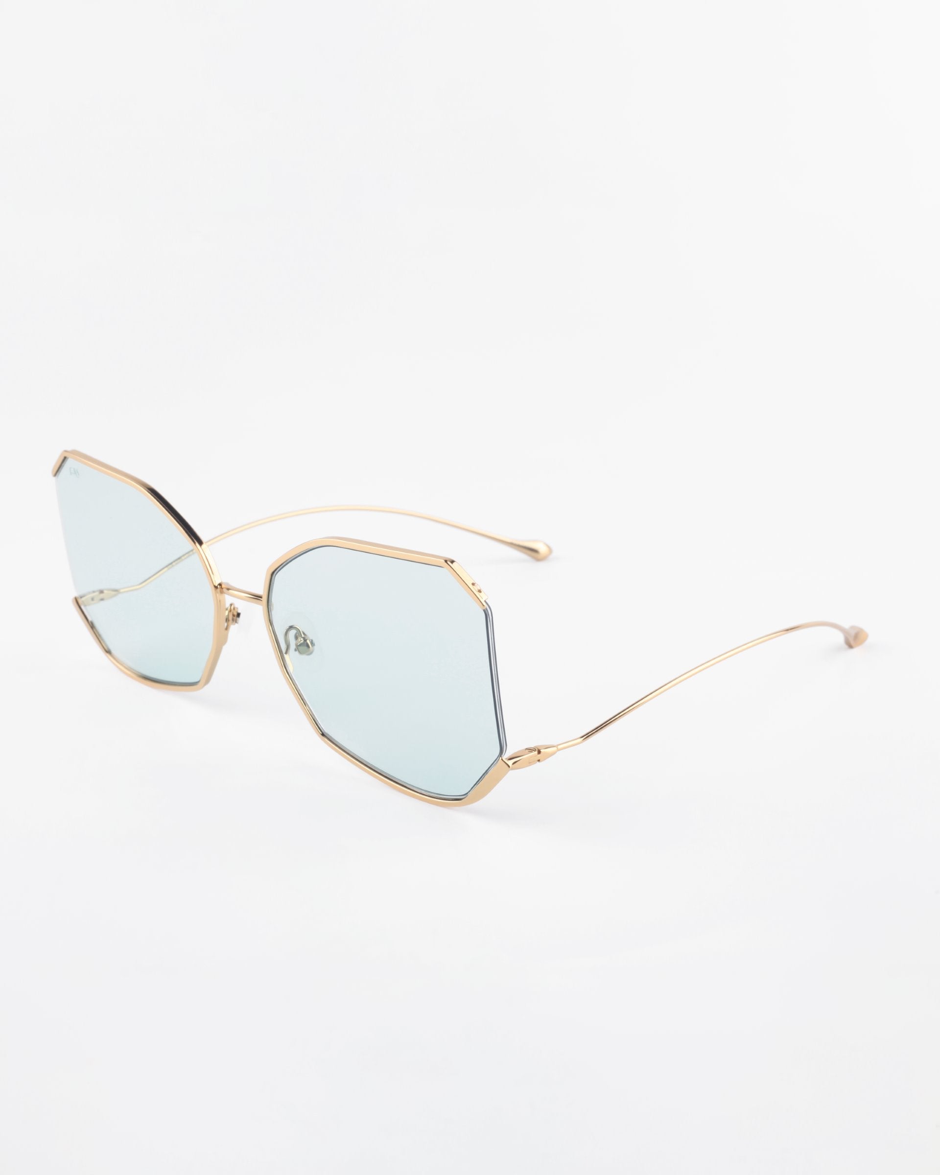 A pair of stylish eyeglasses with a geometric, hexagonal frame featuring light blue tinted lenses. The Painter by For Art&#39;s Sake® has a thin, gold-plated stainless steel frame and temples with a minimalist and modern design. The ultra-lightweight Nylon lenses offer 100% UVA &amp; UVB protection. They are placed on a plain white background.