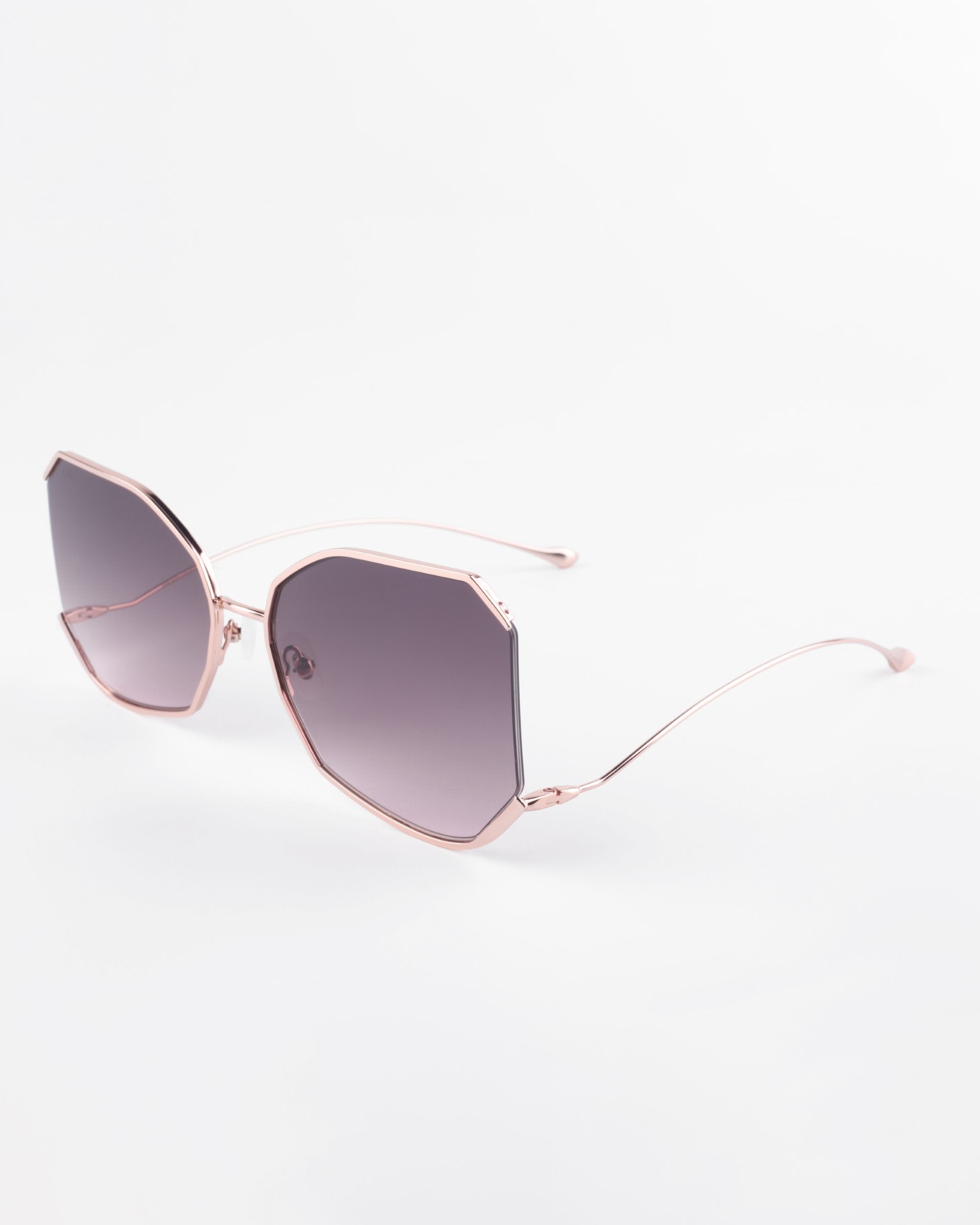 A pair of stylish, oversized Painter sunglasses with a unique hexagonal frame design in rose gold and ultra-lightweight Nylon lenses by For Art&#39;s Sake®. Offering 100% UVA &amp; UVB protection, the gradient lenses transition from dark at the top to lighter at the bottom. The clean, minimalist background emphasizes their elegance.