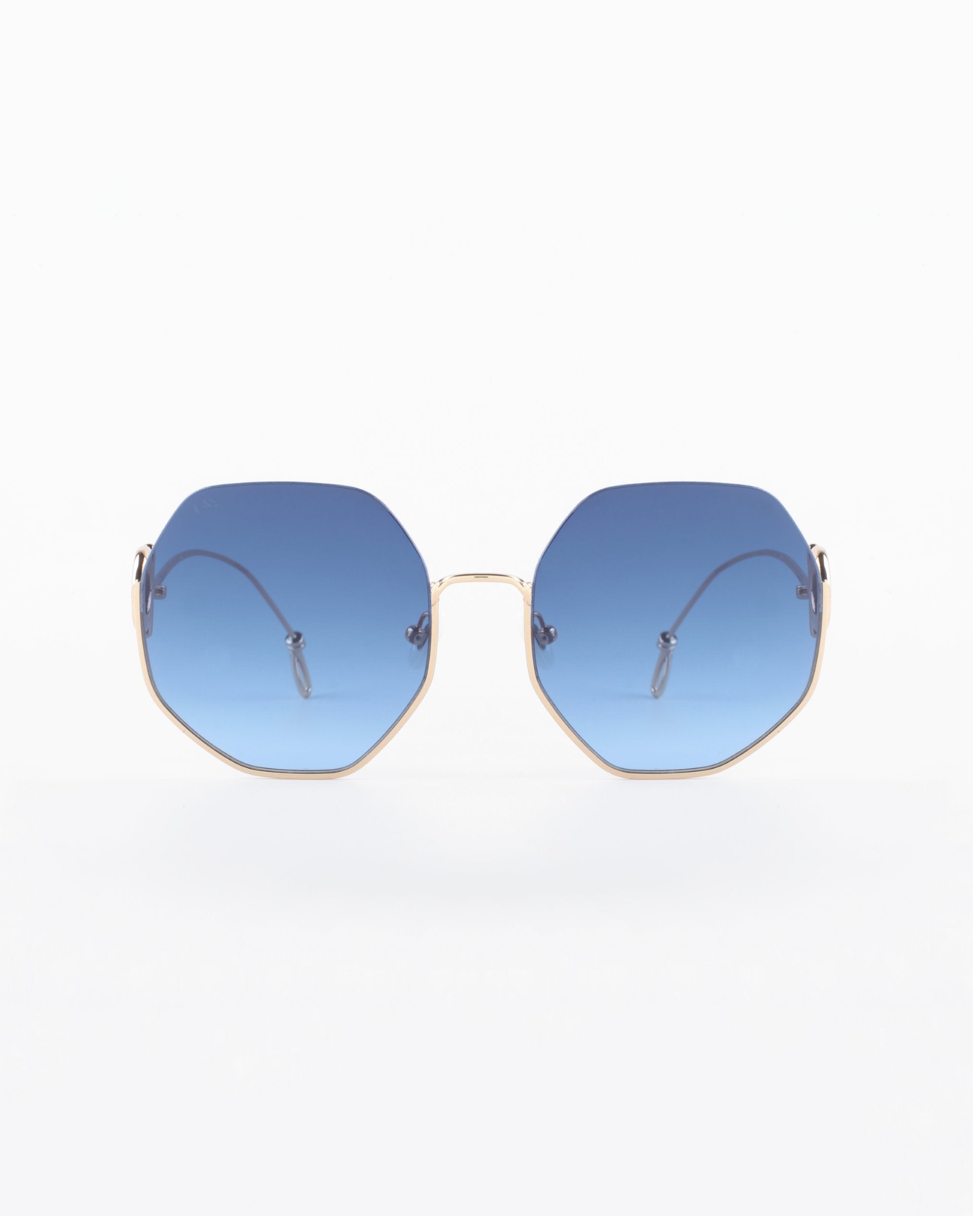 A pair of For Art's Sake® Palace UVA & UVB-protected sunglasses with 18-karat gold-plated wire frames and blue-tinted hexagonal lenses is centered against a white background. The temples extend from the frames to thin, curved earpieces. The overall design is modern and minimalist.