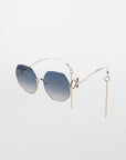 A pair of limited-edition fashionable Palace sunglasses by For Art's Sake® with blue gradient lenses and geometric, 18-karat gold-plated frames. The unique wireframe arms feature decorative chains hanging from the ends, adding an avant-garde touch to the design. These UVA & UVB-protected Palace sunglasses are set against a plain white background.