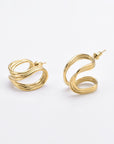 A pair of 24k gold, twisted hoop earrings with a smooth and shiny finish. Each Portrait Earrings Gold by For Art's Sake® features a unique, wavy design with an interwoven loop pattern. The earrings have standard posts for pierced ears and are displayed against a plain white background.