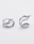 A pair of modern silver earrings with a looping, abstract design. The earrings have a glossy finish and are displayed against a plain white background. Each earring consists of a continuous curved shape with an attached stud for securing to the ear, reminiscent of **Portrait Earrings Silver by For Art's Sake®**.