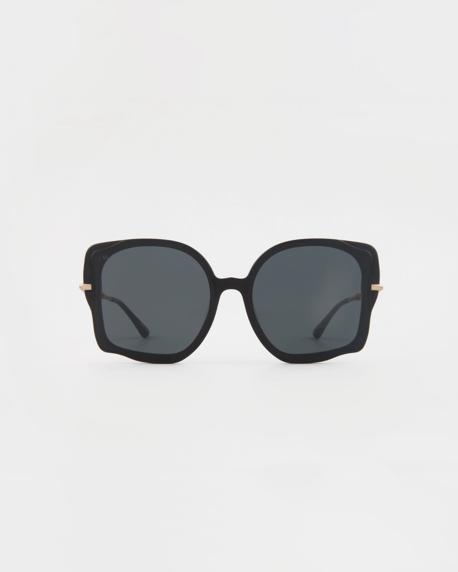 The Fahrenheit by For Art&#39;s Sake®: A pair of oversized square sunglasses with black frames and dark tinted lenses. These handmade acetate sunglasses feature thin 18-karat gold-plated accents on the outer sides of each lens, connecting to slender black arms. The background is plain white.