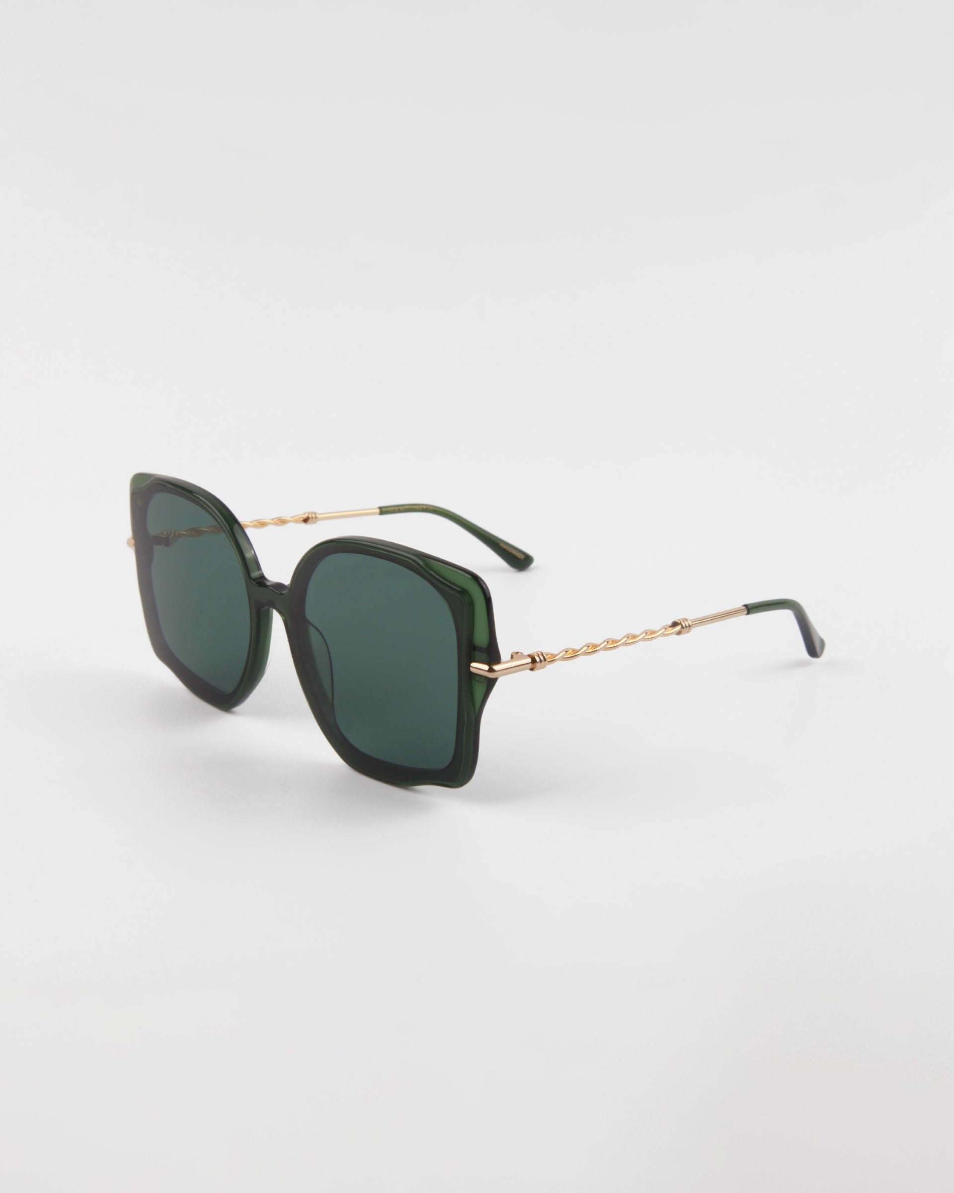 A pair of stylish, oversized square-shaped For Art&#39;s Sake® Fahrenheit sunglasses with dark green lenses and matching green frames. The temples feature 18-karat gold-plated chain detail connecting to the green earpieces, adding an elegant touch to the design. The handmade acetate sunglasses are displayed on a plain white background.