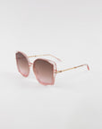 Square-shaped, oversized frame Fahrenheit sunglasses by For Art's Sake® with pink gradient lenses and a light pink metal frame, featuring thin 18-karat gold-plated arms with a chain-like design. The Fahrenheit sunglasses by For Art's Sake® are placed on a plain white background.