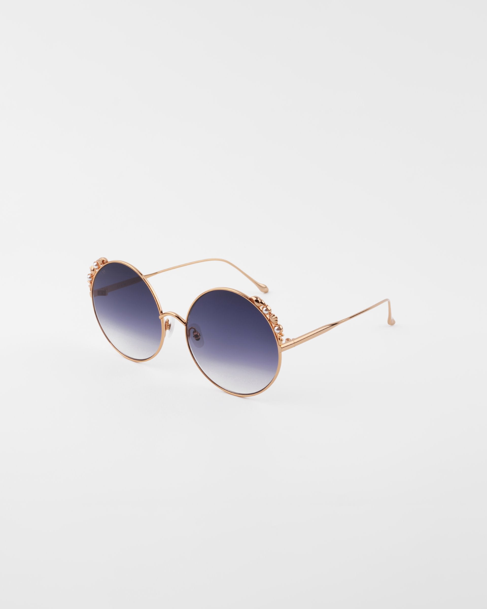 Round sunglasses with gold-colored frames and blue gradient lenses. Handmade gold-plated detailing adorns the top of the lenses. The ultra-lightweight shatter resistant lenses are 100% UVA & UVB-protected, ensuring both style and safety. The Lindy by For Art's Sake® is positioned against a plain white background.