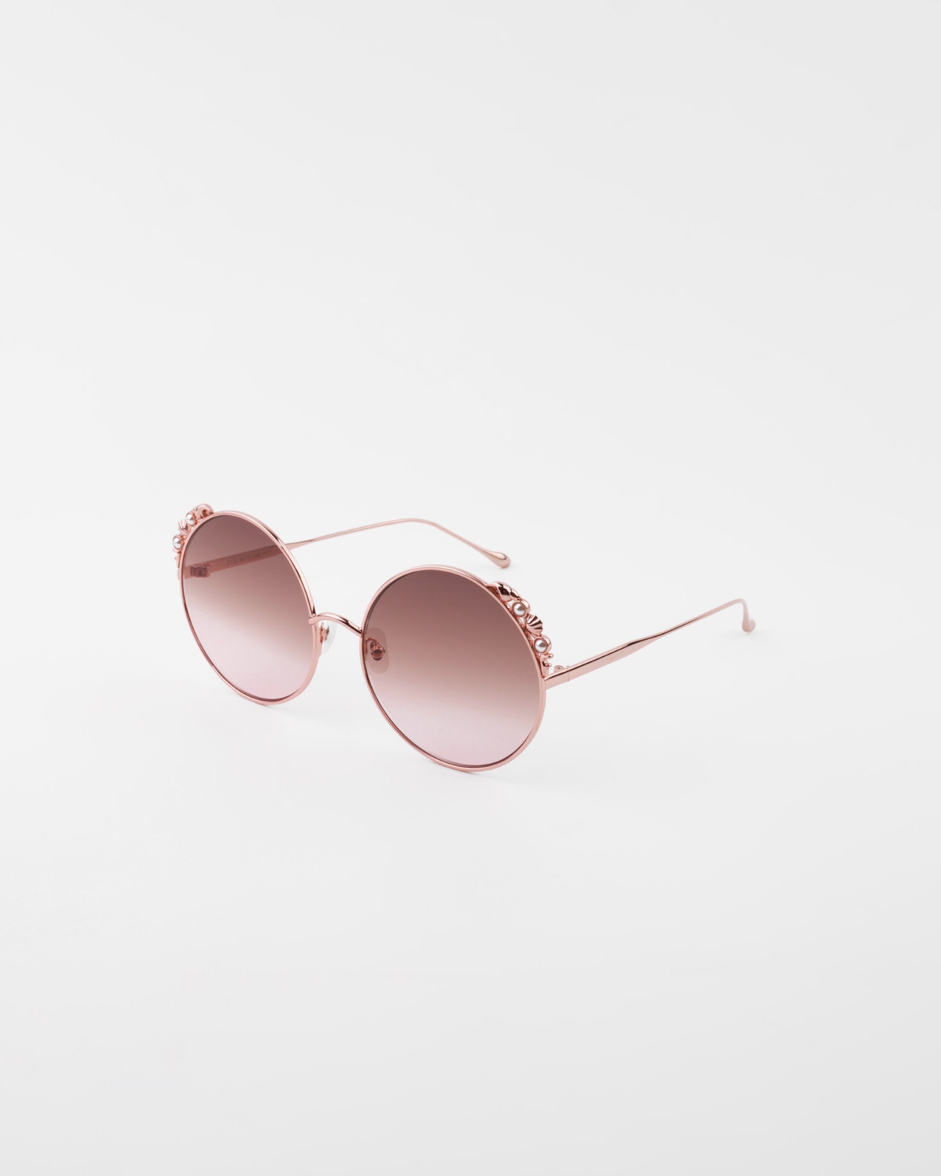 A pair of stylish round sunglasses with ultra-lightweight shatter-resistant pink-tinted lenses and rose gold frames featuring floral detailing on the upper rims, offering 100% UVA &amp; UVB protection, the Lindy by For Art&#39;s Sake®.