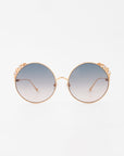 A pair of For Art's Sake® Lindy handmade gold-plated sunglasses with ultra-lightweight shatter resistant lenses that transition from dark blue at the top to clear at the bottom. The temples are thin and gold, while the decorative rim around the lenses adds a touch of elegance. 100% UVA & UVB-protected. Background is white.