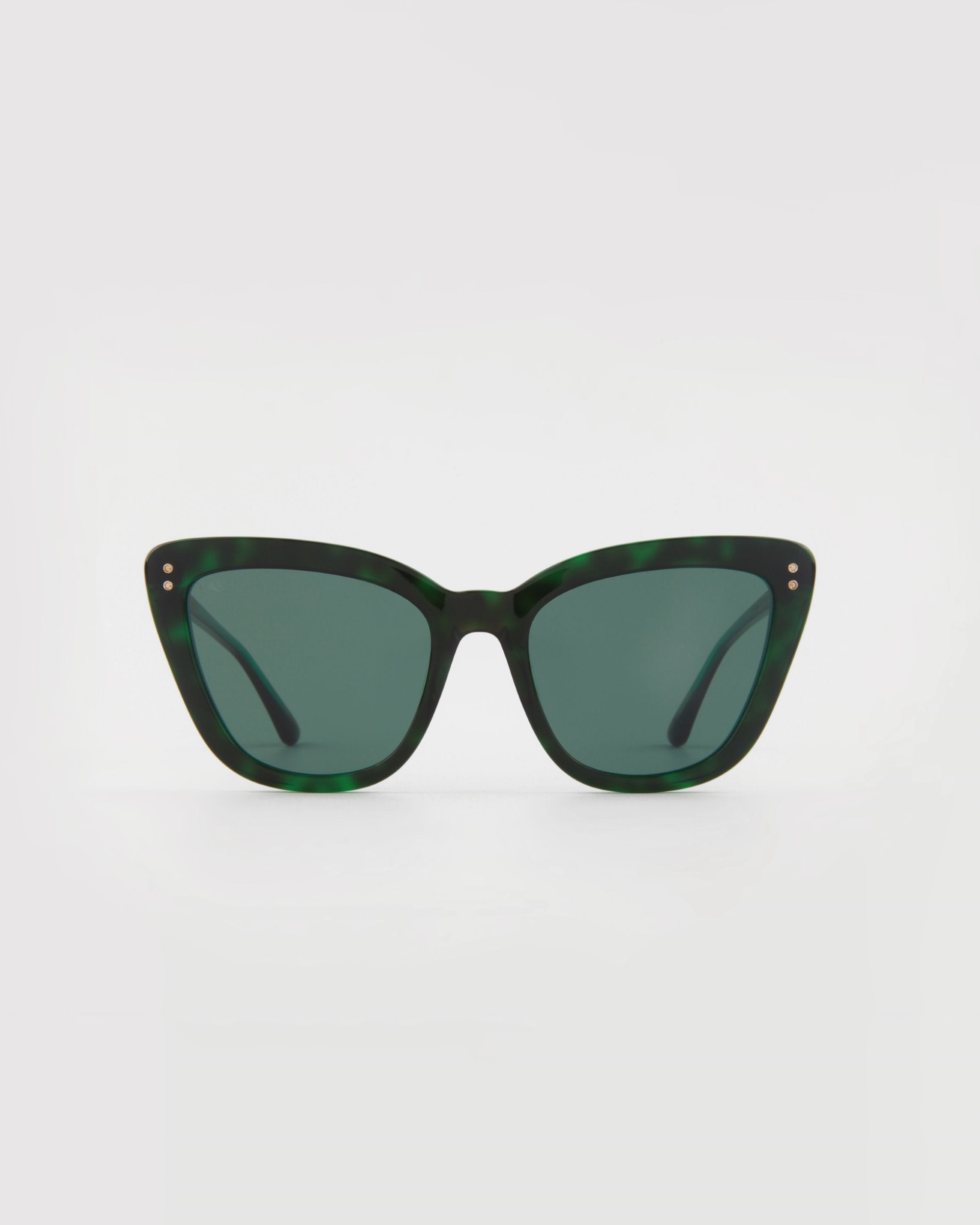 A pair of **Ice Cream by For Art&#39;s Sake®** sunglasses with cat-eye frames in dark green tortoiseshell and dark lenses is centered against a plain, light background. The glasses have a slight upturn at the outer corners, metal accents near the hinges, and offer UVA &amp; UVB protection.