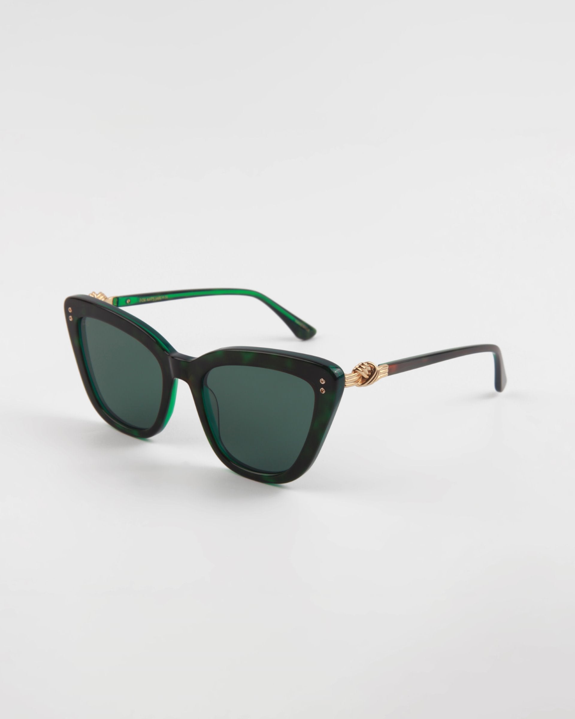 A pair of stylish, dark green cat-eye frames crafted from handmade acetate with dark tinted lenses. The arms feature a gold twist detail near the hinges, adding an elegant touch. These Ice Cream sunglasses by For Art&#39;s Sake® provide complete UVA &amp; UVB protection, ensuring both style and safety. The background is plain white.
