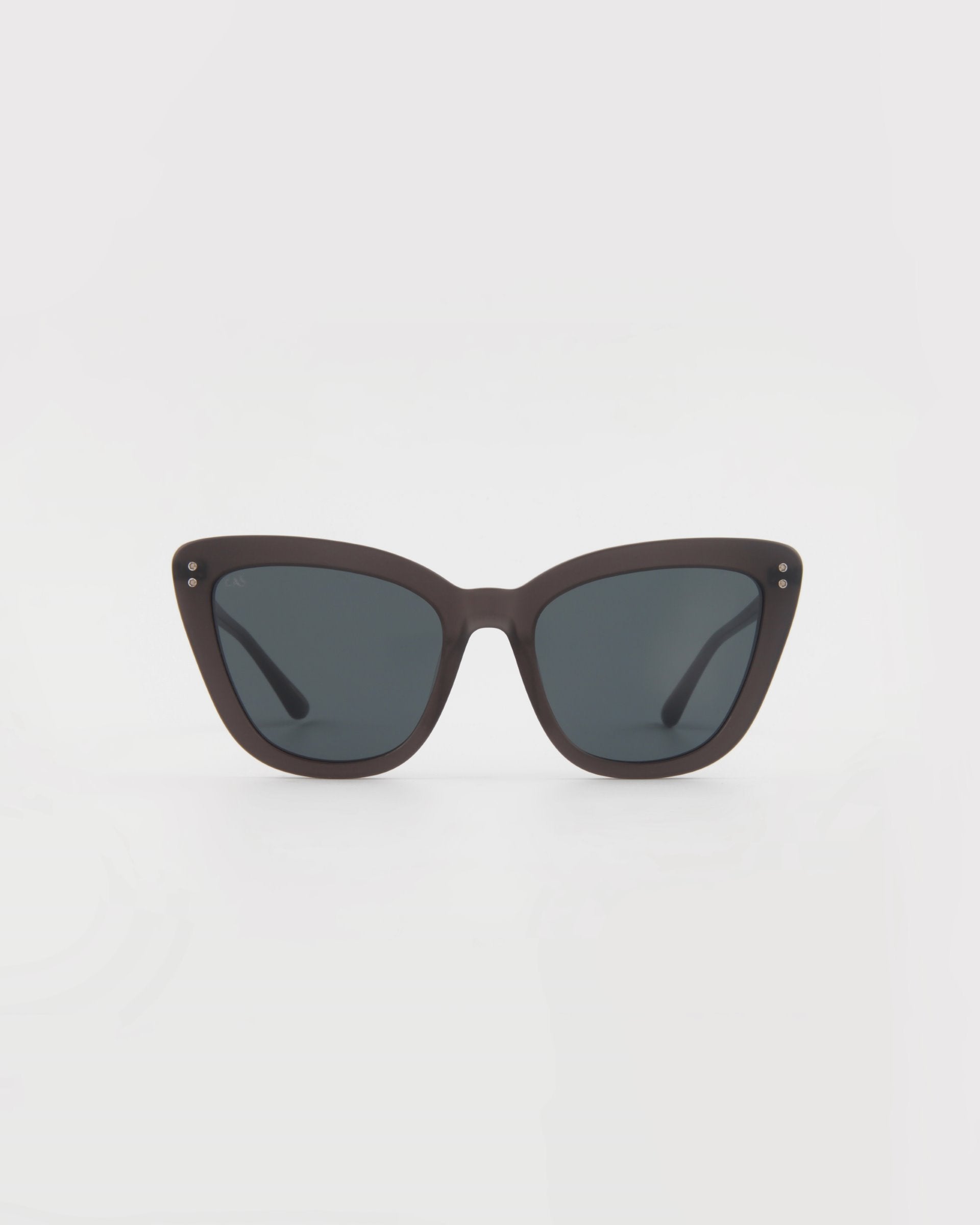 A pair of black For Art's Sake® Ice Cream sunglasses with dark tinted lenses, viewed from the front. The sunglasses have a sleek, matte finish with small metal stud details near the hinges on the corners of the frames. Handmade acetate cat-eye frames ensure both style and quality, set against a plain white background.
