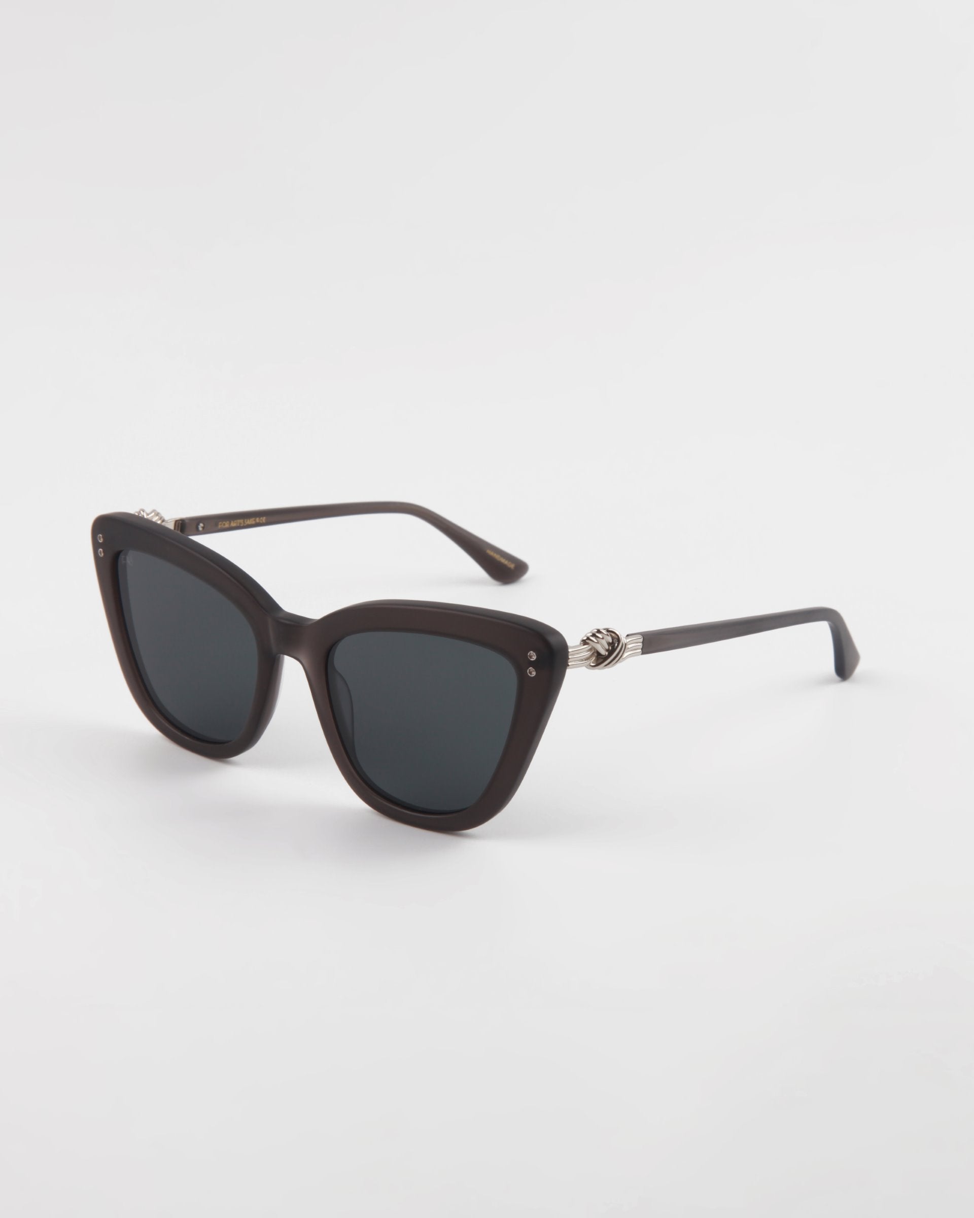 A pair of stylish black cat-eye Ice Cream frames with dark tinted lenses. These handmade acetate sunglasses by For Art&#39;s Sake® feature a slightly thick frame, small metallic accents on the temples, and provide complete UVA &amp; UVB protection. The background is plain white.