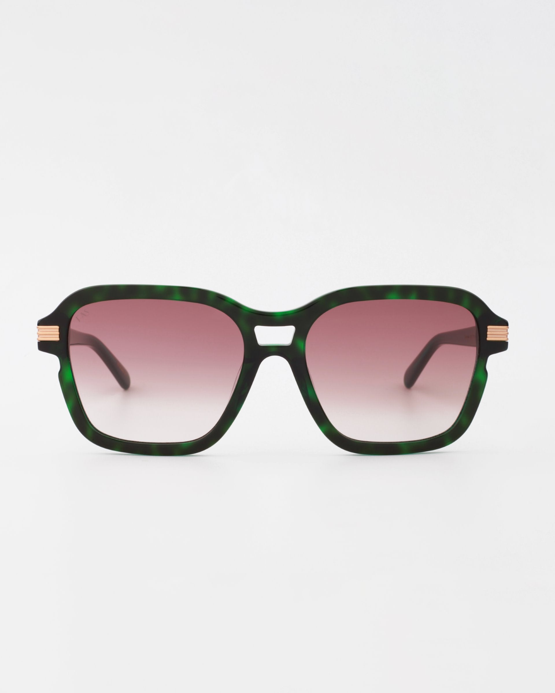 A pair of Shadyside sunglasses by For Art&#39;s Sake® with green tortoiseshell frames and shatter-resistant nylon lenses transitioning from pink to clear. The arms are thin and black, accented with gold-plated temple detail near the hinges. Set against a plain white background.