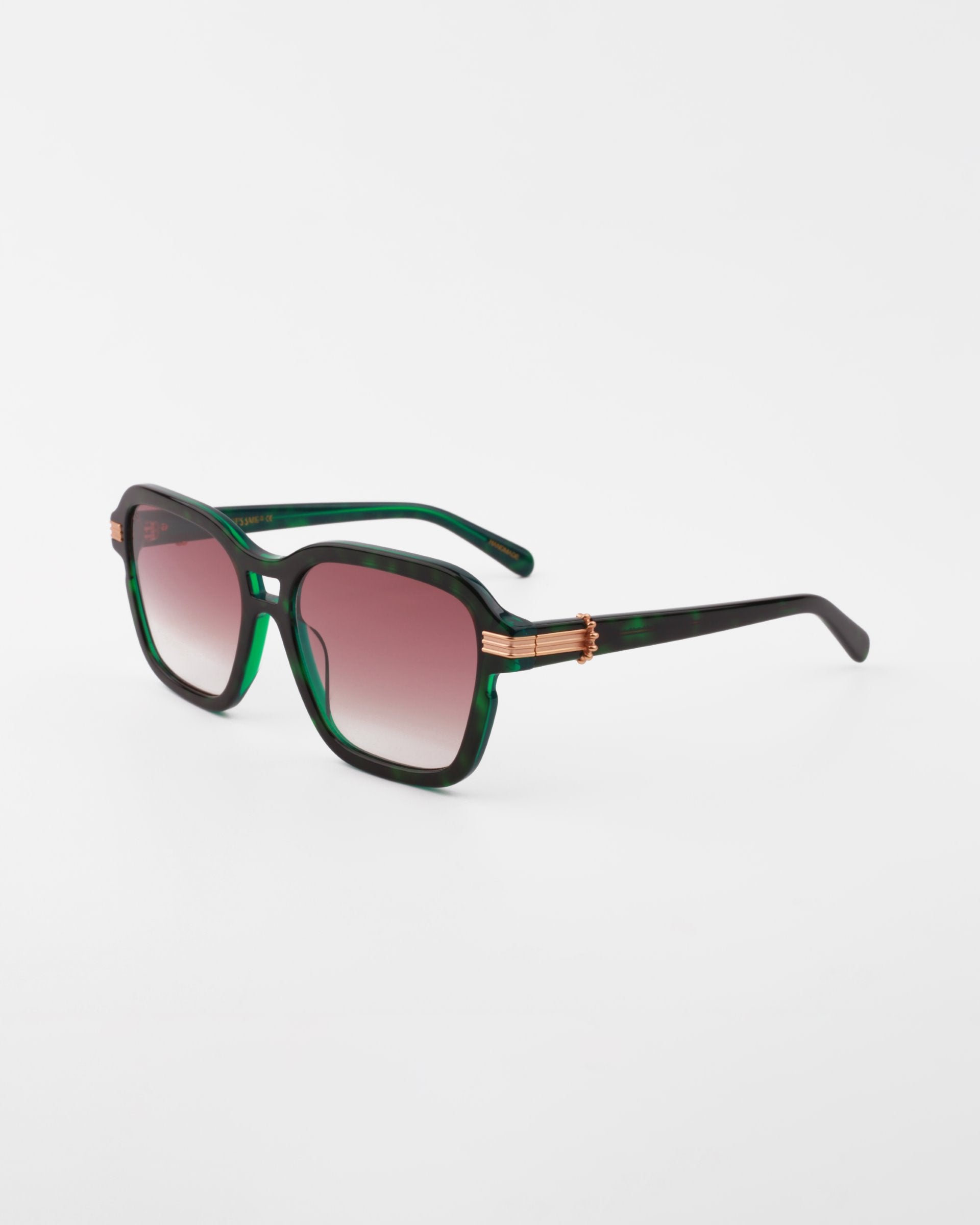 Rectangular gradient green and black Shadyside sunglasses by For Art's Sake® with gold-plated temple detail, positioned on a reflective white surface. The lenses feature a brown gradient tint and are made from shatter-resistant nylon.