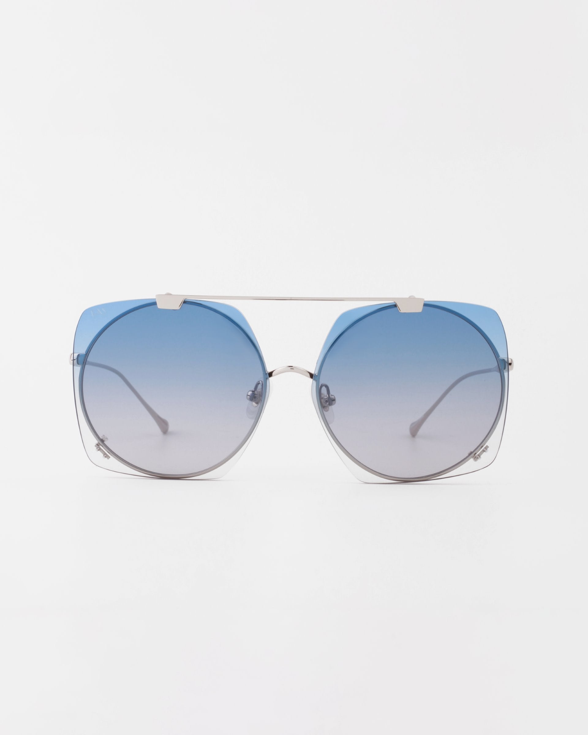 A pair of stylish For Art&#39;s Sake® Last Summer sunglasses with large, round, gradient lenses that fade from dark blue at the top to clear at the bottom. The UVA &amp; UVB-protected glasses feature thin, silver metal frames and a double bridge design. The background is plain white.