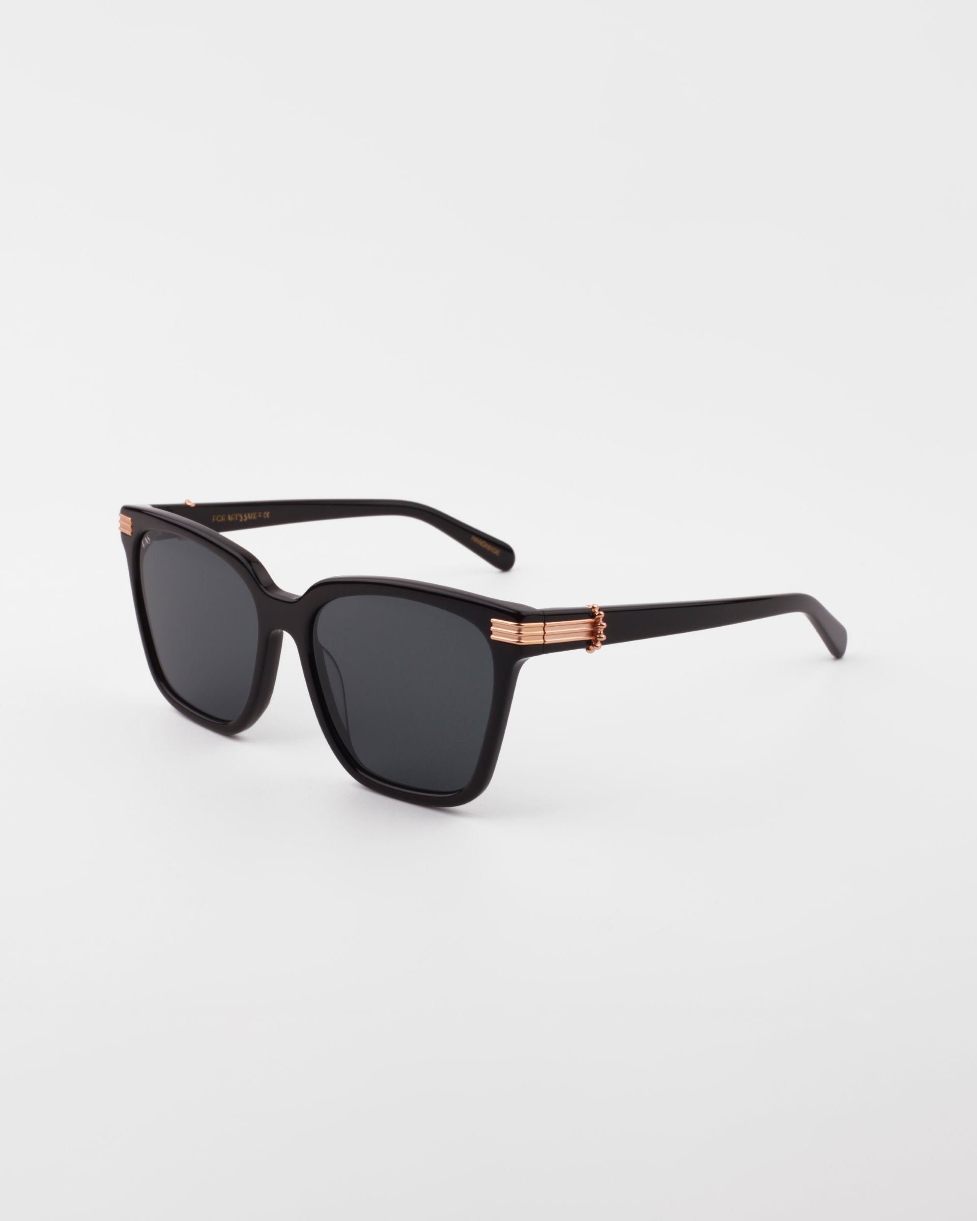 A pair of black rectangular Gaia sunglasses from For Art&#39;s Sake® with UV-protected dark lenses and 18-karat gold-plated accents on the temple hinges, set against a plain white background.