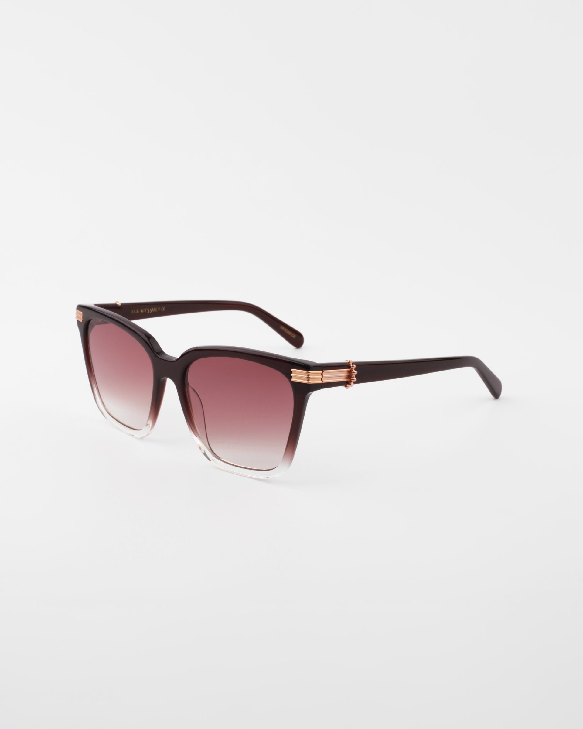 A pair of stylish maroon square-shaped sunglasses with gradient UV-protected lenses. The Gaia by For Art’s Sake® glasses feature 18-karat gold-plated temples and dark-colored arms. Handmade acetate sunglasses that boast a sleek, modern design, set against a plain white background.