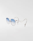 A pair of For Art's Sake® Birthday Cake sunglasses with round, thin gold-plated frames and blue gradient, UV-protected lenses is displayed against a plain white background. The arms of the glasses are uniquely designed with curled ends and decorative loops, giving a modern, artistic look.