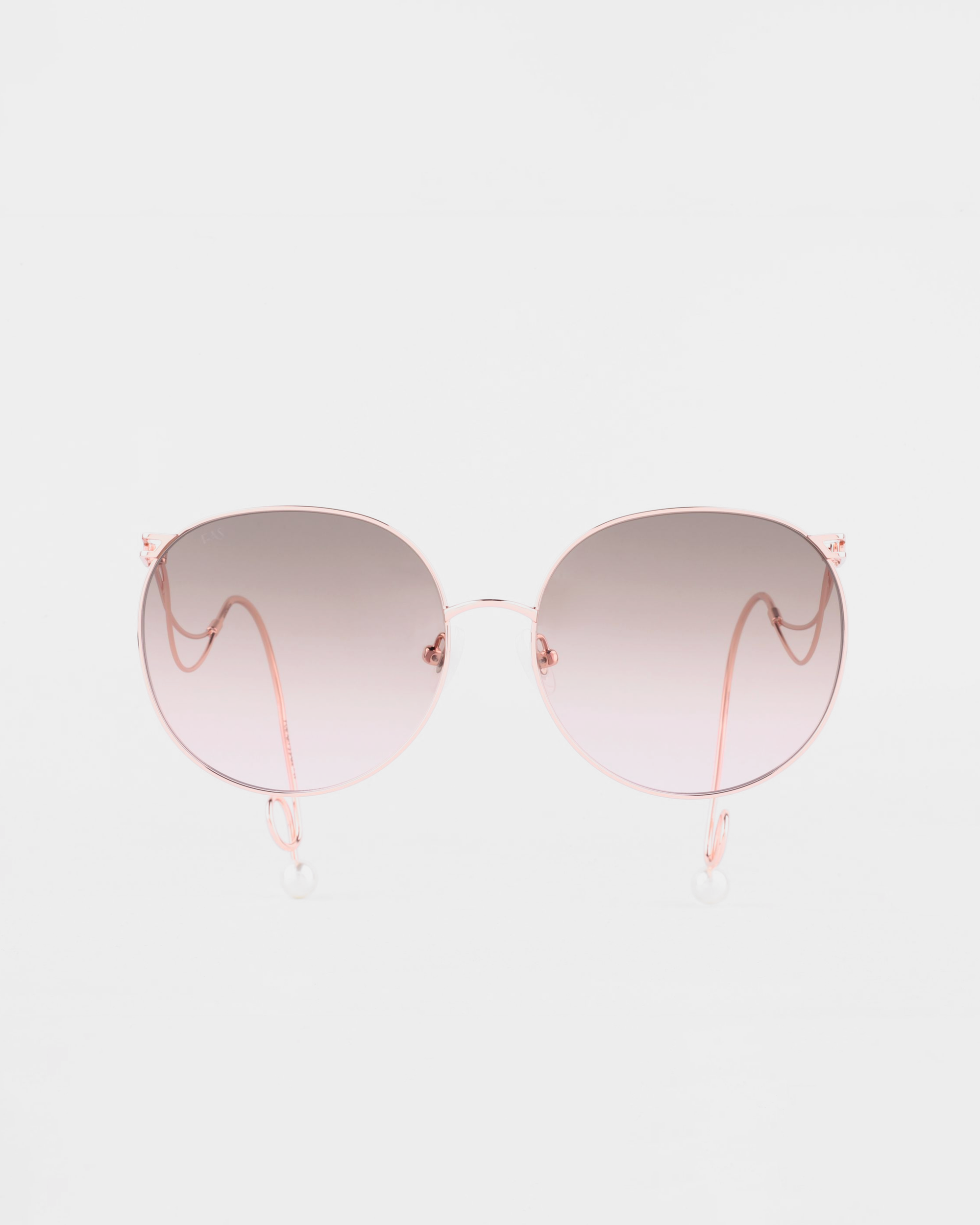 A pair of For Art's Sake® Birthday Cake sunglasses with handmade gold-plated, rose gold frames and gradient lenses that transition from light pink at the bottom to darker pink at the top. The UVA & UVB-protected, shatter-resistant lenses offer clear sight while delicate, curved arms and clear nose pads add elegance. The background is plain white.