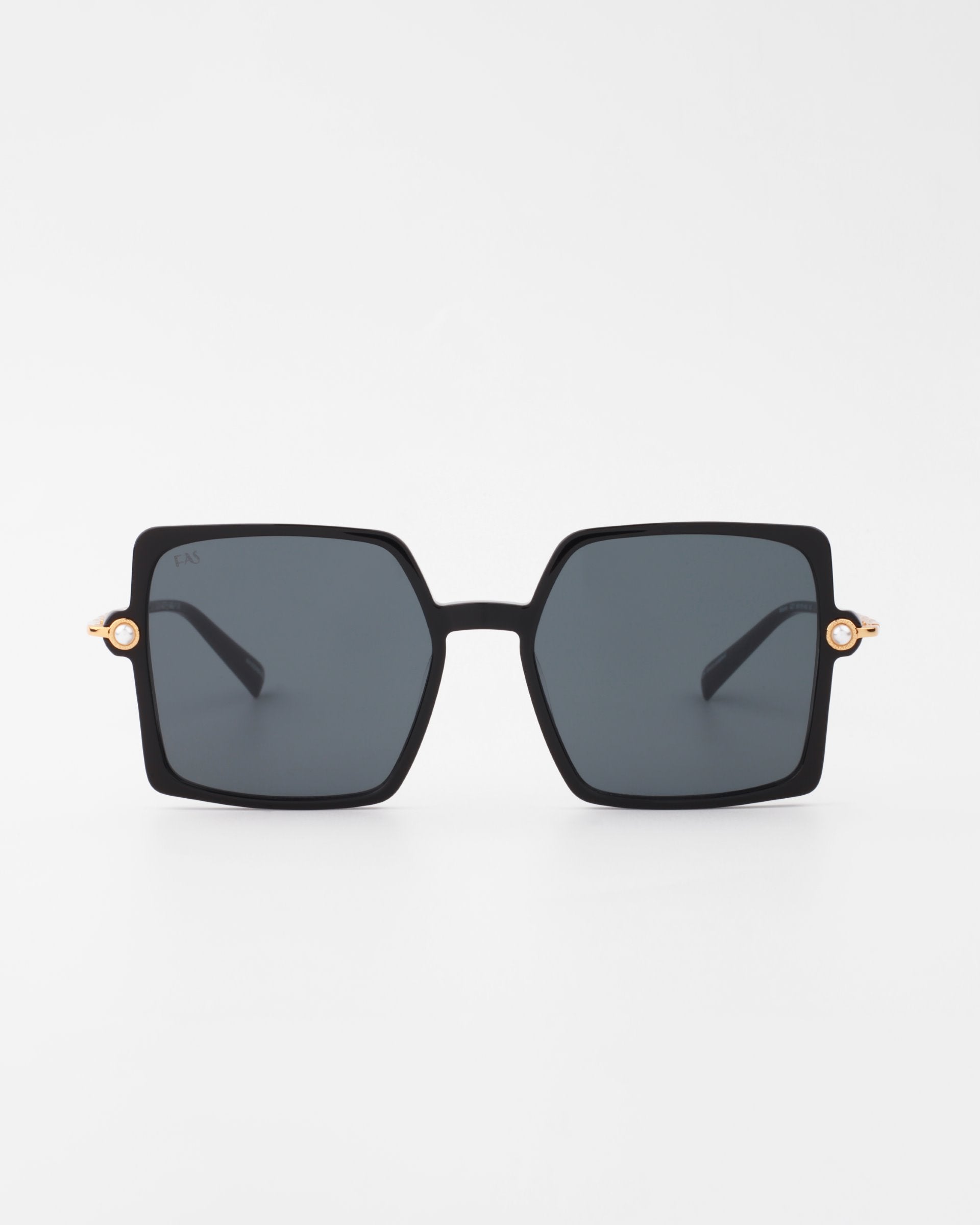 A pair of large, square-shaped sunglasses with black frames and dark lenses. The temples are sleek, featuring 18-karat gold-plated arms and a small gold accent on the hinges. Handmade acetate Moxie by For Art's Sake® offering UVA & UVB protection, the overall design is modern and stylish against a plain white background.