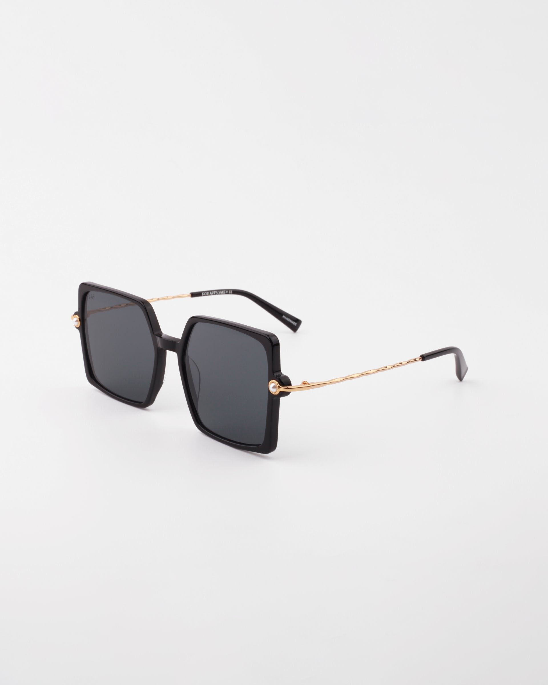 A pair of Moxie by For Art's Sake® black square-shaped handmade acetate sunglasses featuring 18-karat gold-plated arms. The twisted design of the arms leads to black ear tips. Dark lenses provide full UVA & UVB protection, and the sunglasses are photographed against a white background.