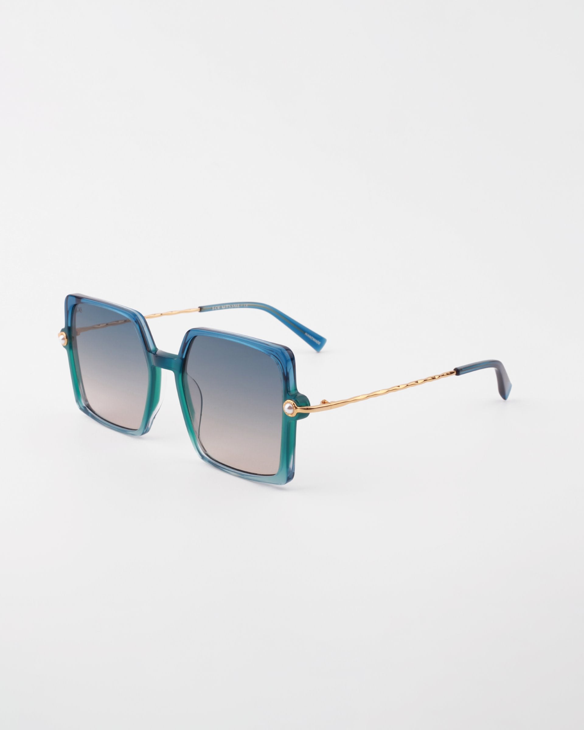 Square-shaped handmade acetate Moxie sunglasses by For Art&#39;s Sake® with gradient green and blue frames and 18-karat gold-plated temples on a white background. The lenses are tinted, transitioning from light to dark towards the top, offering UVA &amp; UVB protection. The temple tips are dark blue.