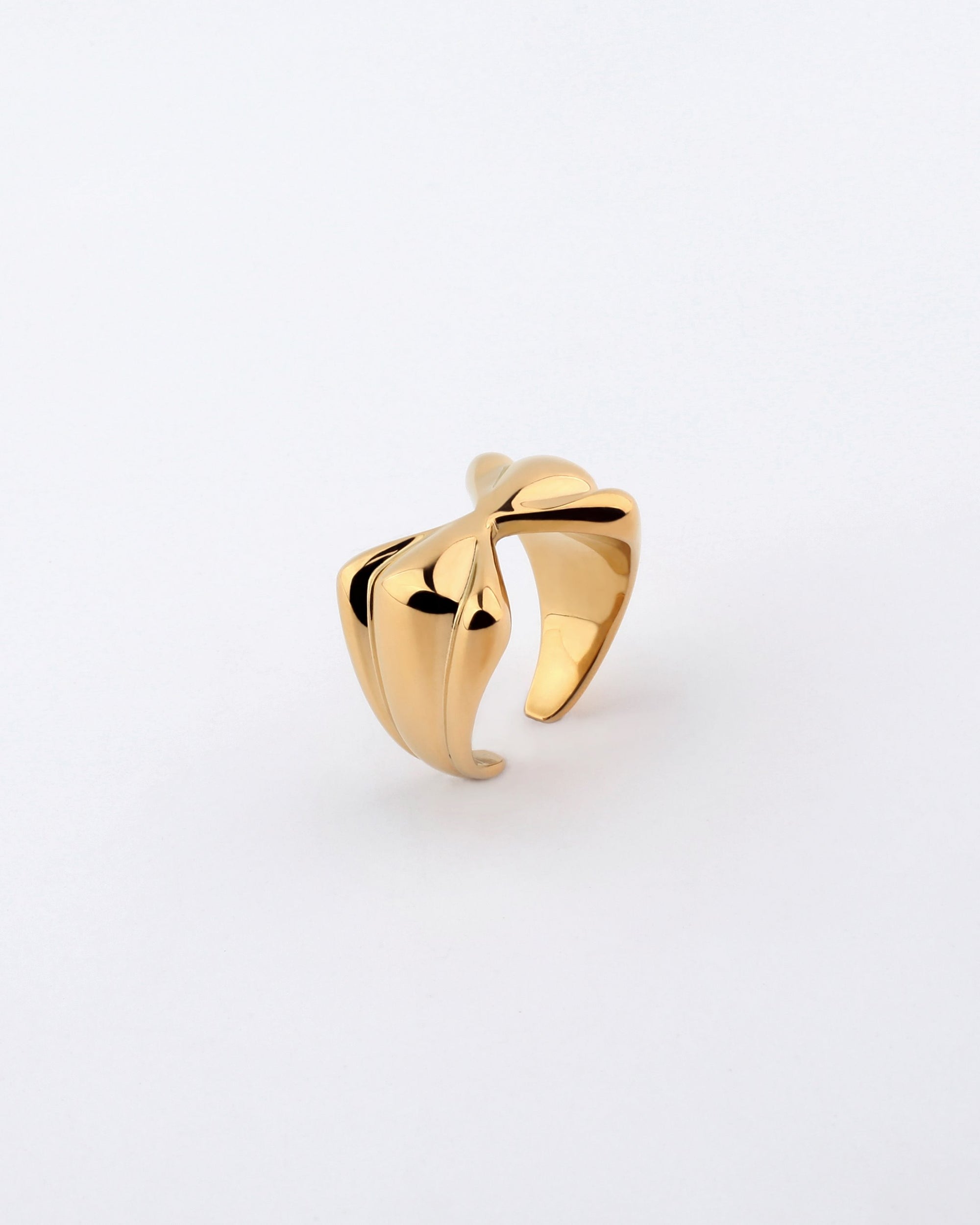 The Sydney Ring by For Art&#39;s Sake® is a polished gold-plated piece featuring a modern, sculptural design with an asymmetrical twisted form against a plain white background. The smooth and reflective surface of this ring highlights its elegant and contemporary style, subtly reminiscent of a bow-shaped design.